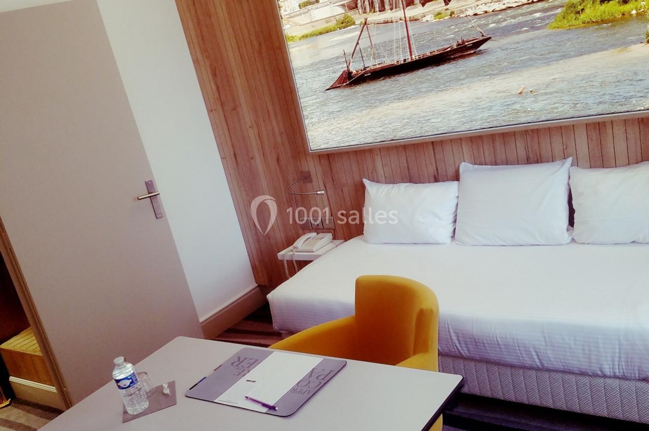 Chambre lumineuse avec un lit simple, un bureau, une chaise jaune et une grande photo murale représentant une rivière.