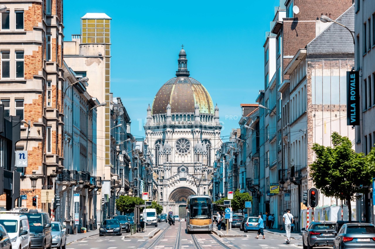 Rue bruxelloise avec tramway, façades haussmanniennes et synagogue de la Régence au fond.