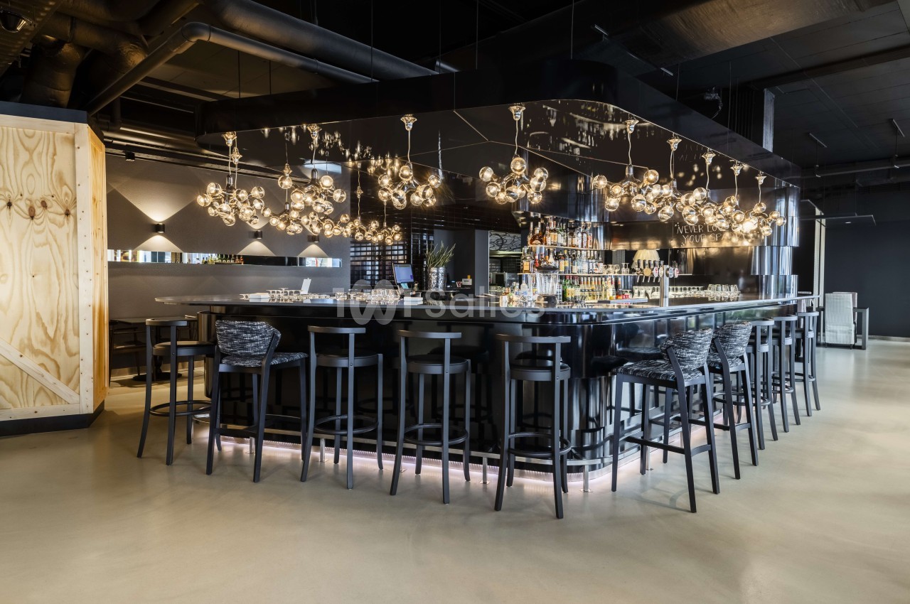 Comptoir de bar longiligne noir avec tabourets assortis, luminaires suspendus design et plafond industriel.