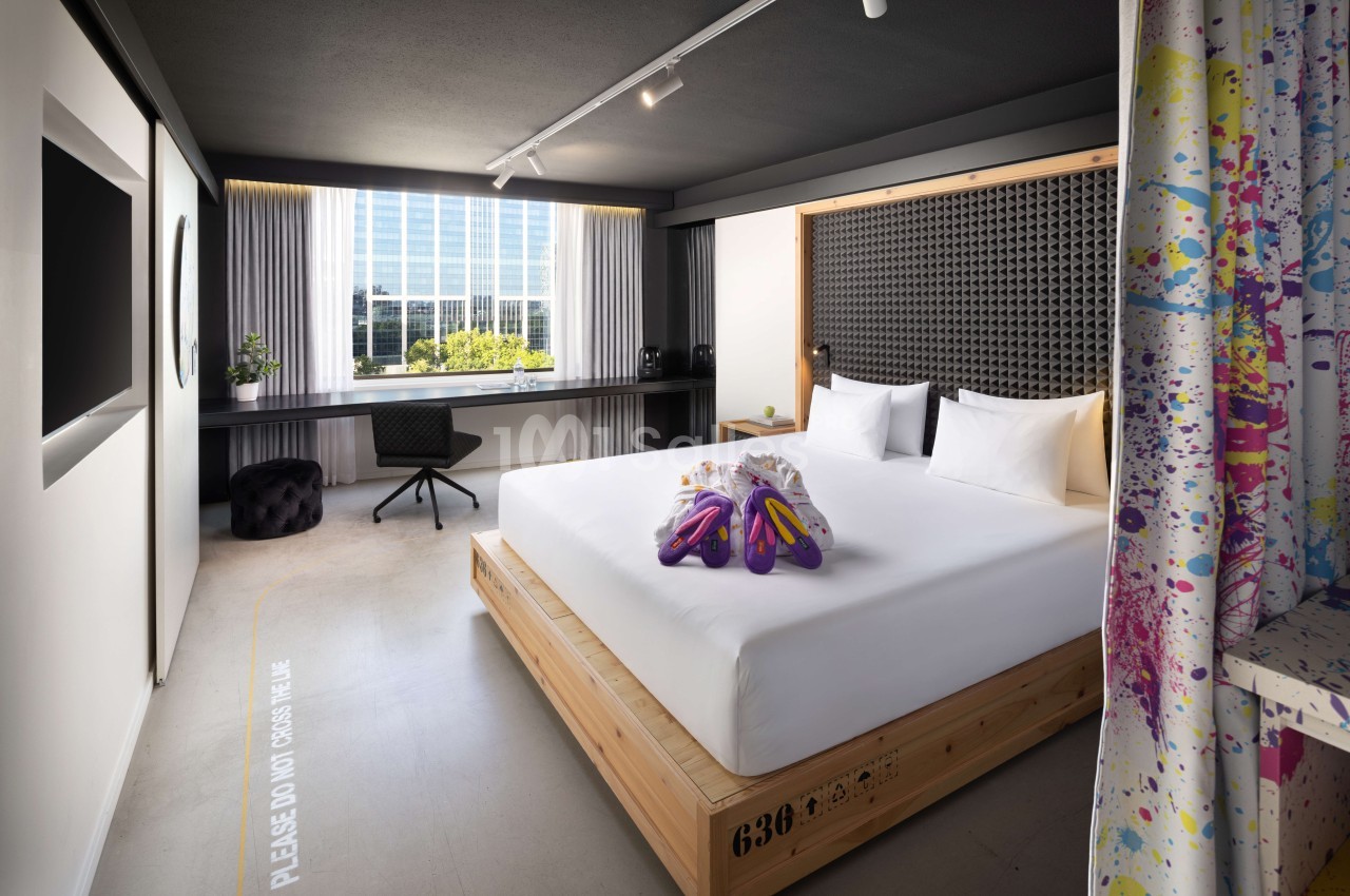Chambre d'hôtel design avec lit double, bureau près de la fenêtre et rideaux colorés à motifs floraux.