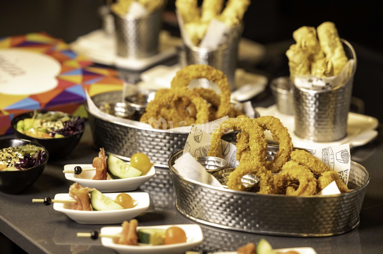 Table dressée avec beignets dorés en paniers argentés, amuse-bouches et décoration colorée.