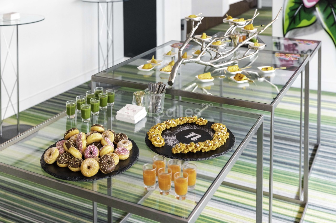 Tables de verre présentant pâtisseries, jus de fruits, verres de cocktail et branche décorée avec amuse-bouches - espace intérieur moderne.