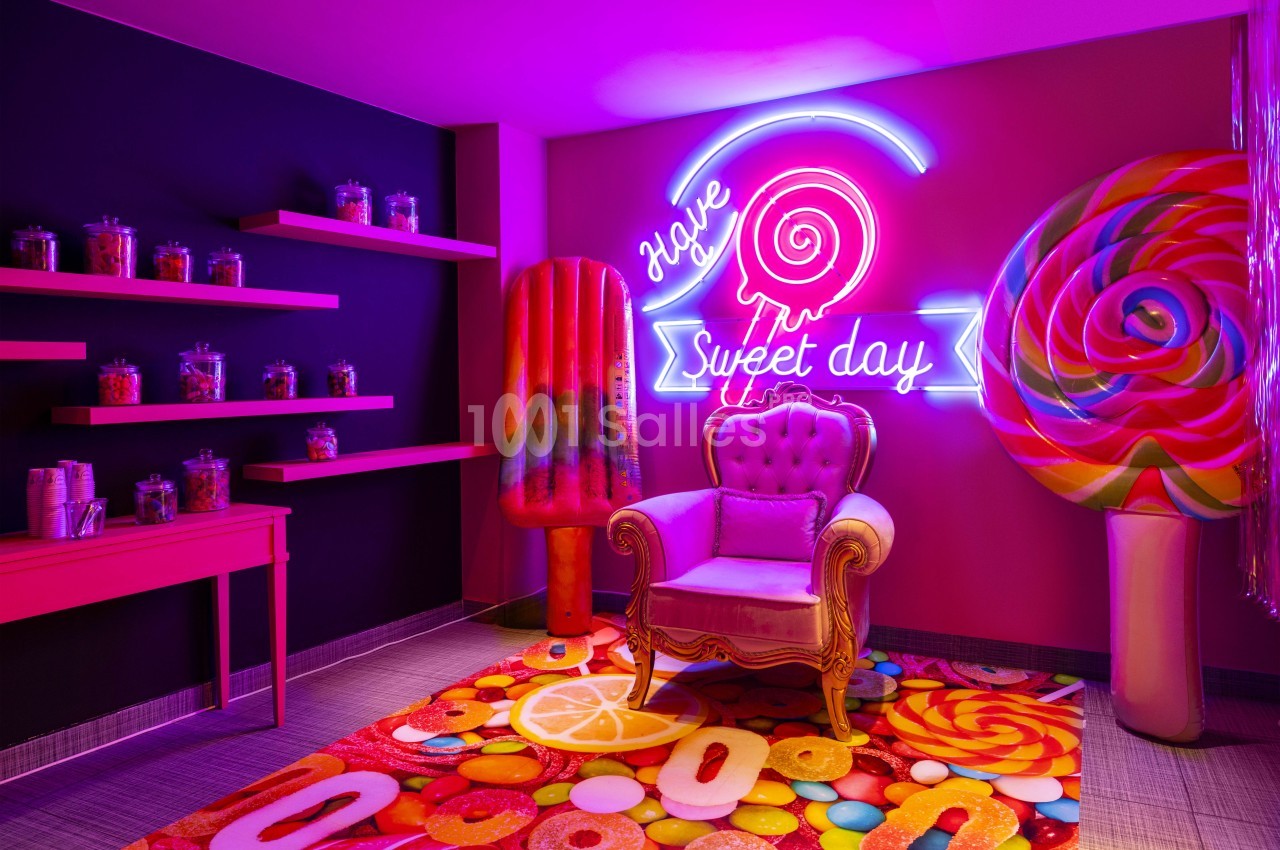 Salle intérieure aux murs magenta - étagères rose fluo, fauteuil velours, enseigne néon, décor sucré au sol.