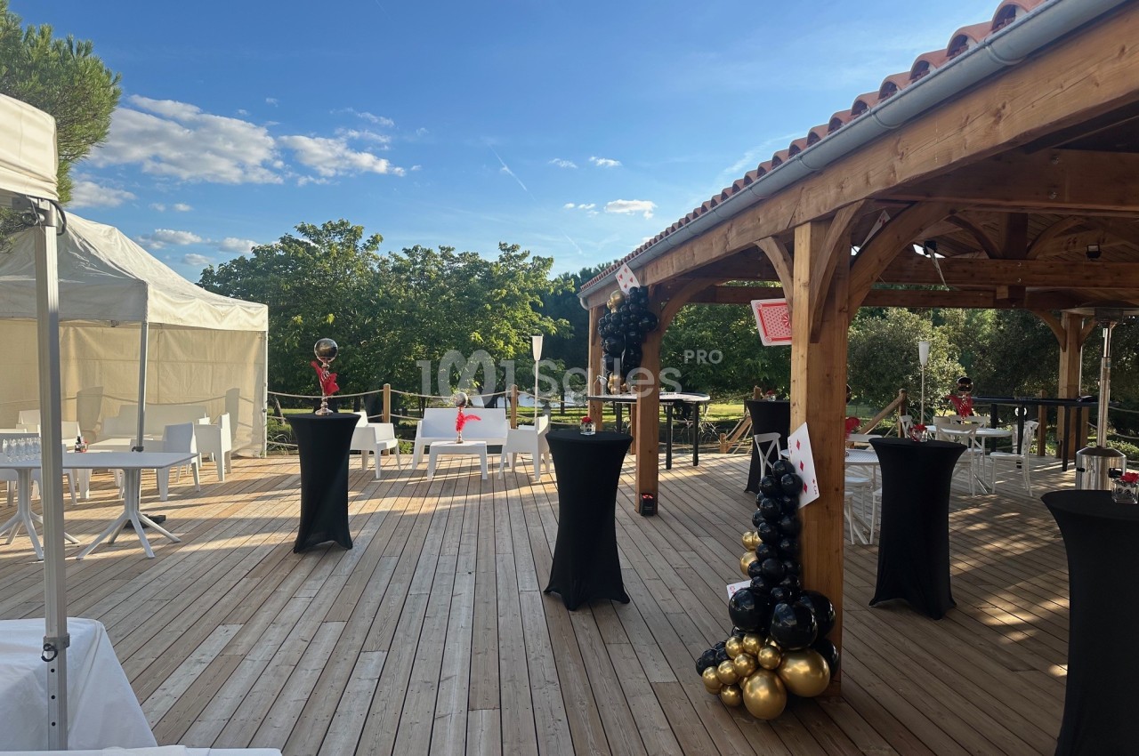 Terrasse en bois aménagée pour événement - charpente bois, tables hautes noires, décoration ballons noir et or.