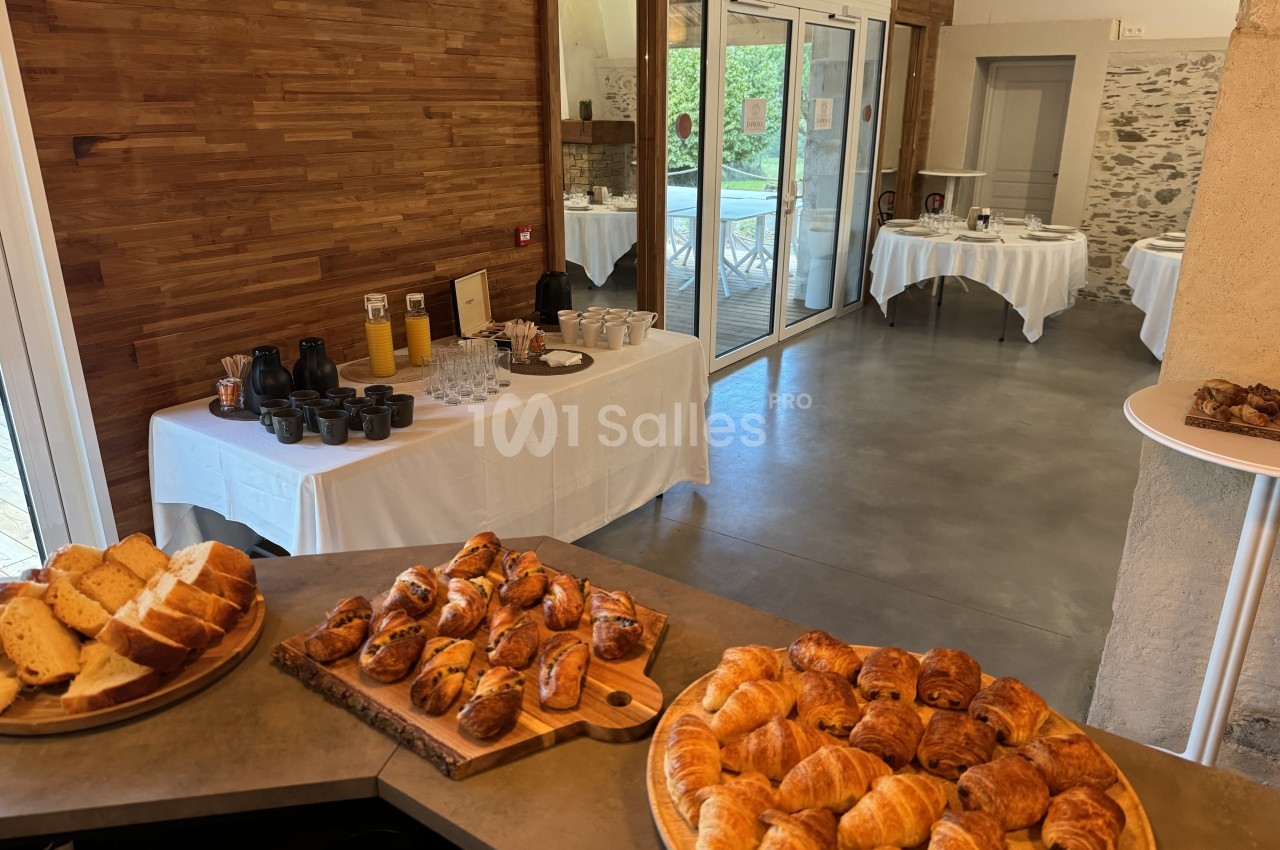 Salle de réception aménagée avec buffet de viennoiseries en avant-plan, tables dressées en arrière-plan et baies vitrées donnant sur la piscine.
