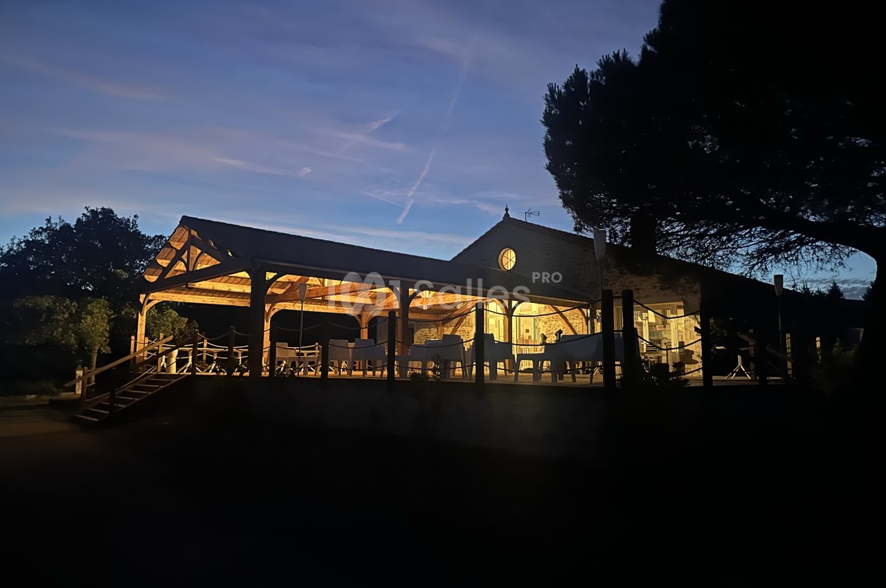 Bâtiment d'accueil en bois éclairé au crépuscule, avec terrasse couverte et escaliers d'accès.