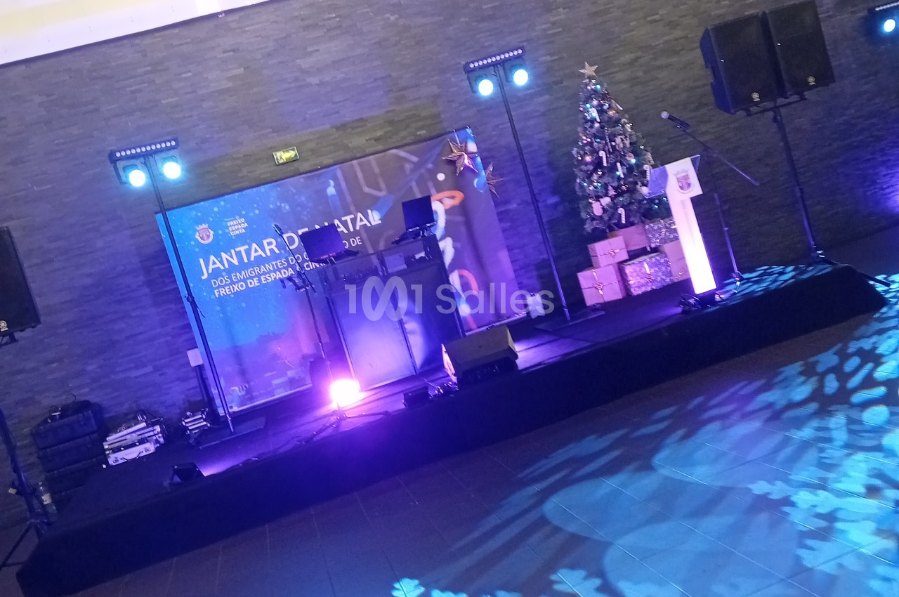 Scène dressée avec podium, écrans, projecteurs bleus et sapin de Noël pour événement festif.