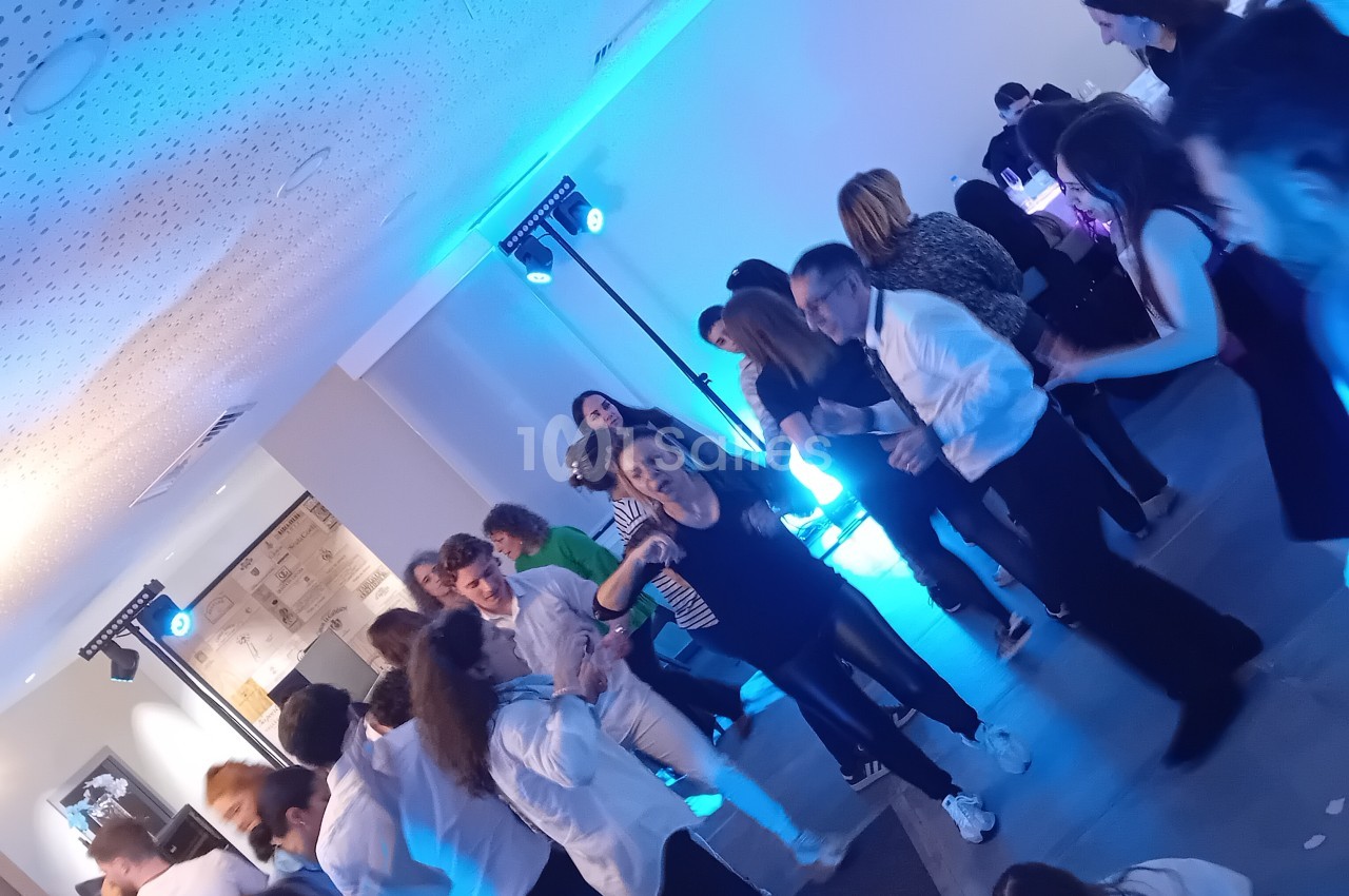 Salle intérieure avec éclairage bleu néon, convives debout et animés autour d'équipements de DJ.