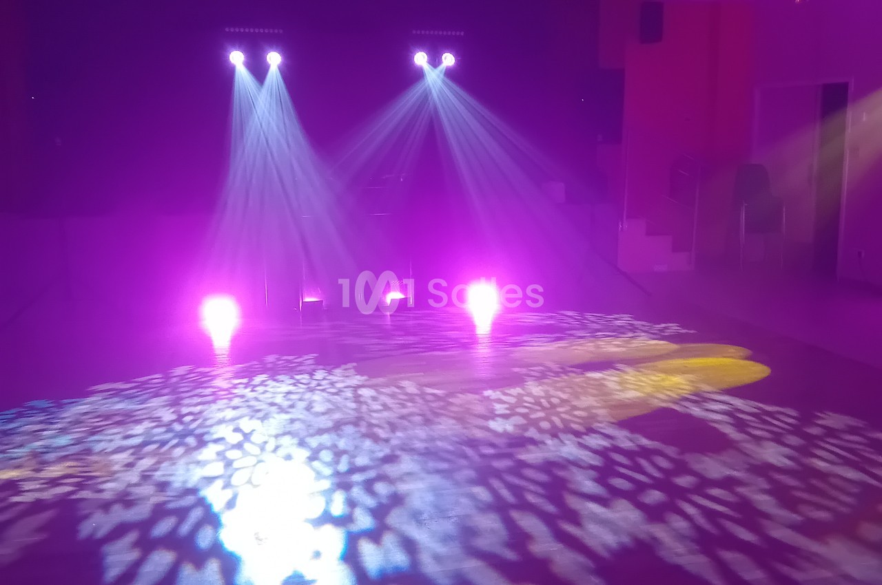 Salle vide avec éclairage de scène violet et rose, projecteurs et jeu de lumière au sol.