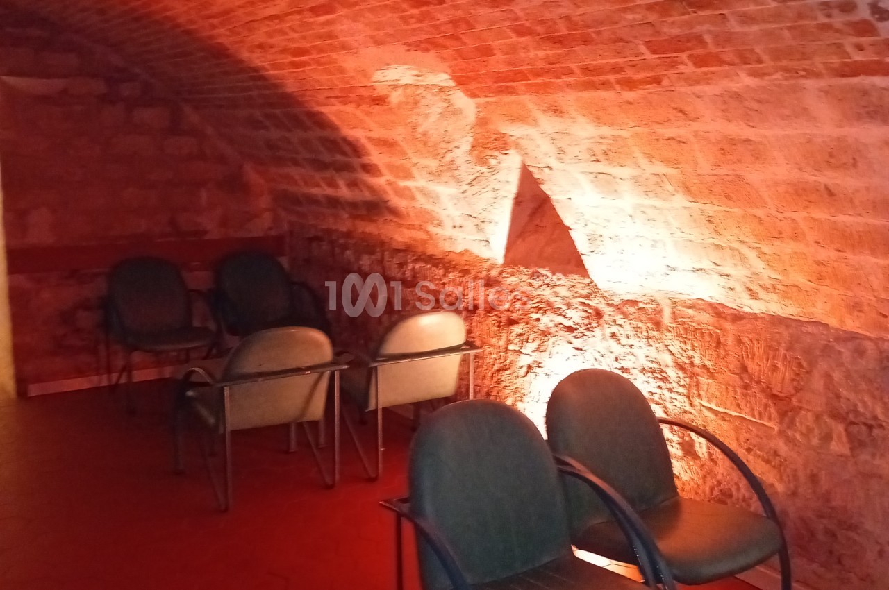 Espace intérieur aux murs en brique rouge avec éclairage ambiant chaud, chaises noires disposées au premier plan.