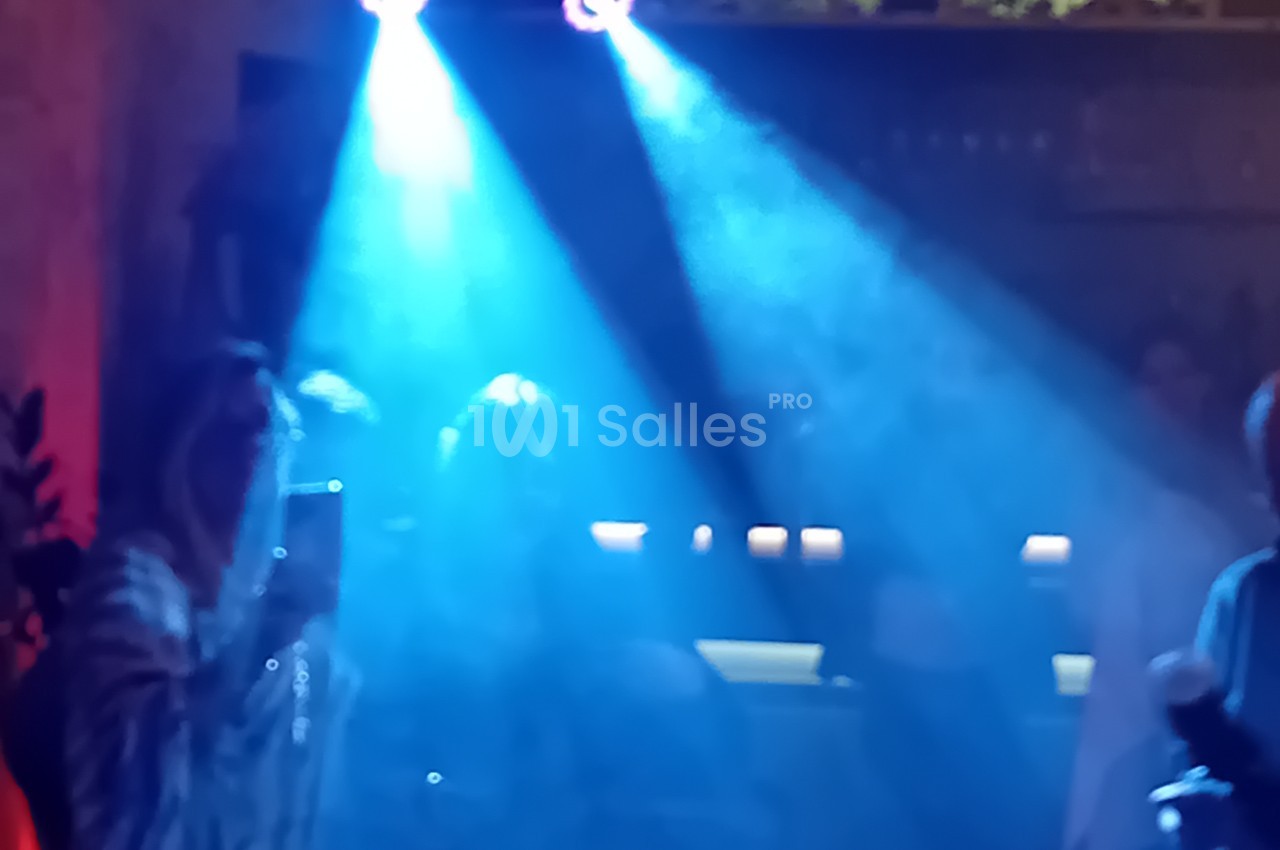 Salle avec projecteurs bleu et blanc créant une ambiance de piste de danse - musiciens visibles.