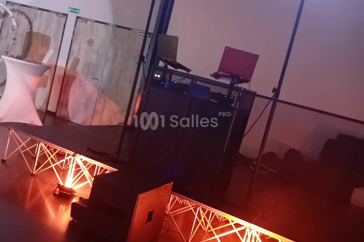 Salle avec éclairage rouge et rose, platine DJ montée sur scène, structures lumineuses géométriques au sol.
