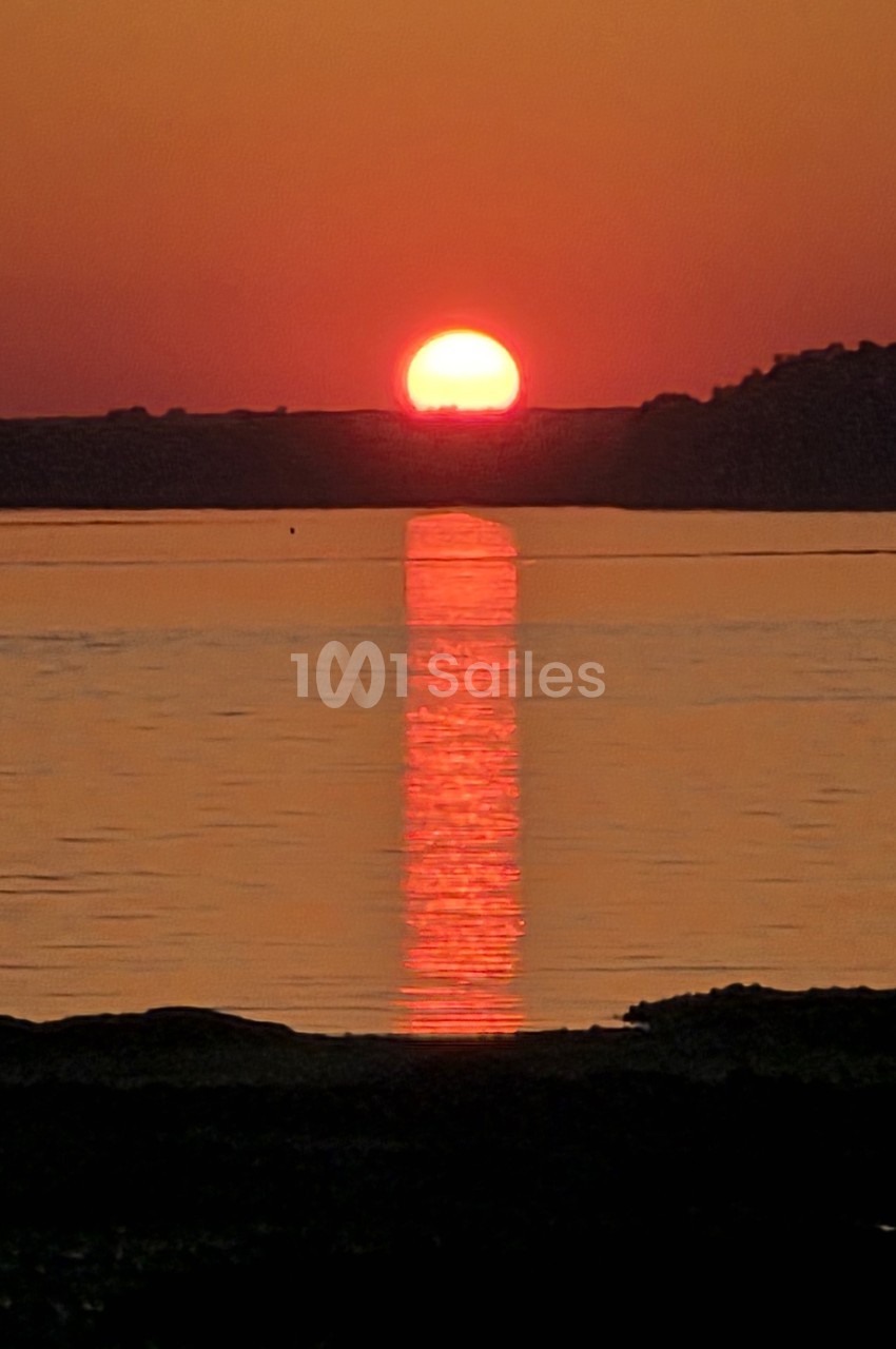Coucher de soleil rouge sur un plan d'eau calme avec boisés en arrière-plan.