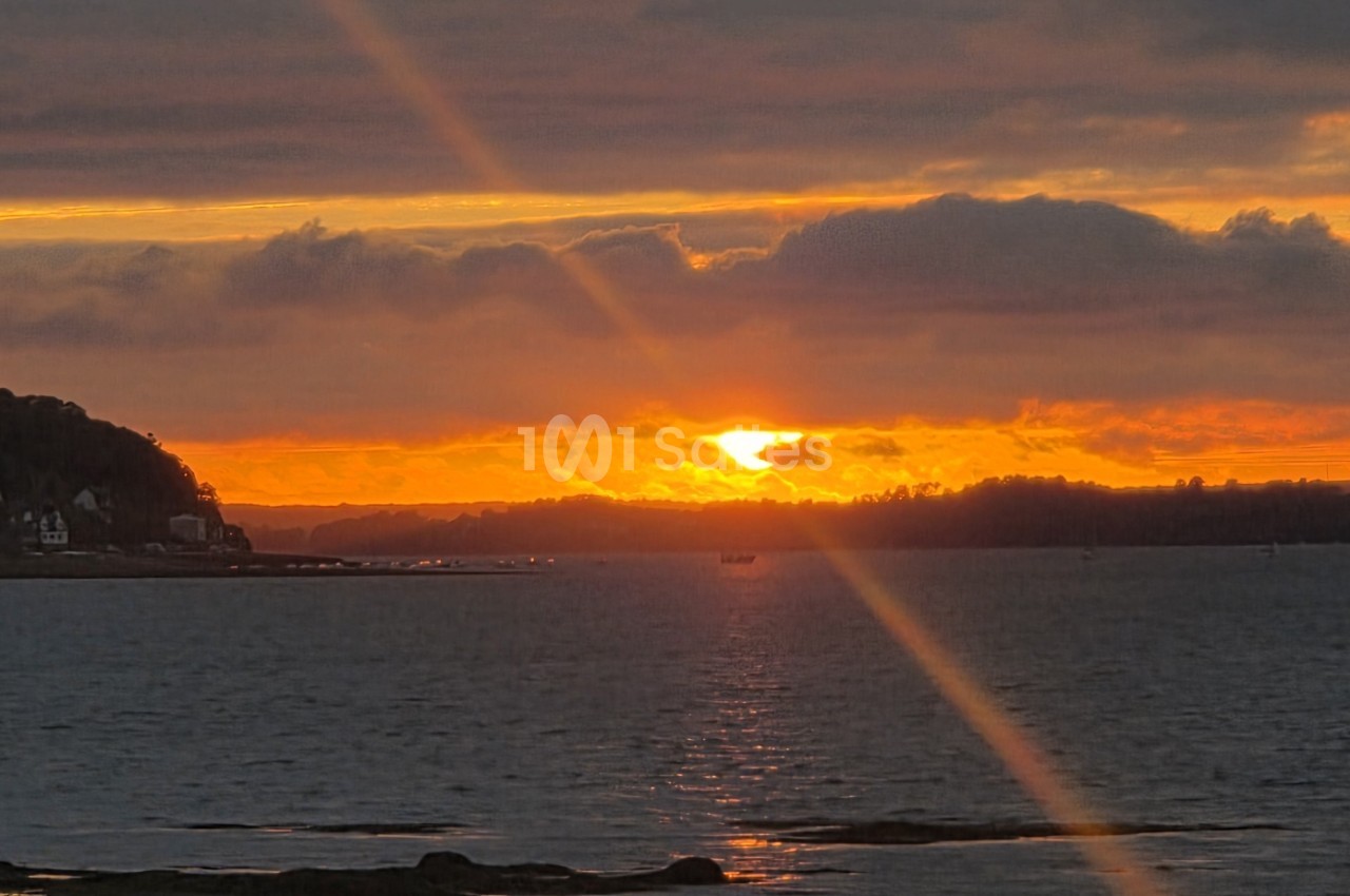 Coucher de soleil sur la baie avec ciel orange doré, nuages et silhouettes boisées des rives.
