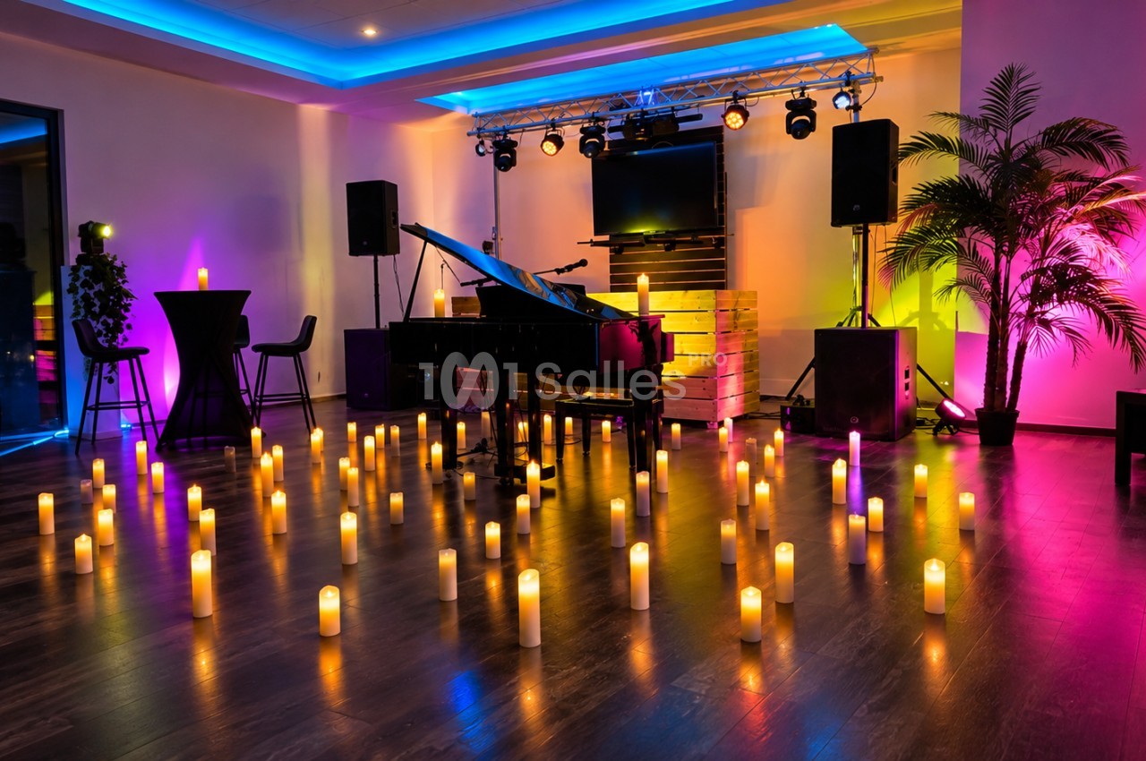 Salle de réception aménagée avec piano, scène, éclairages multicolores et bougies sur le sol.