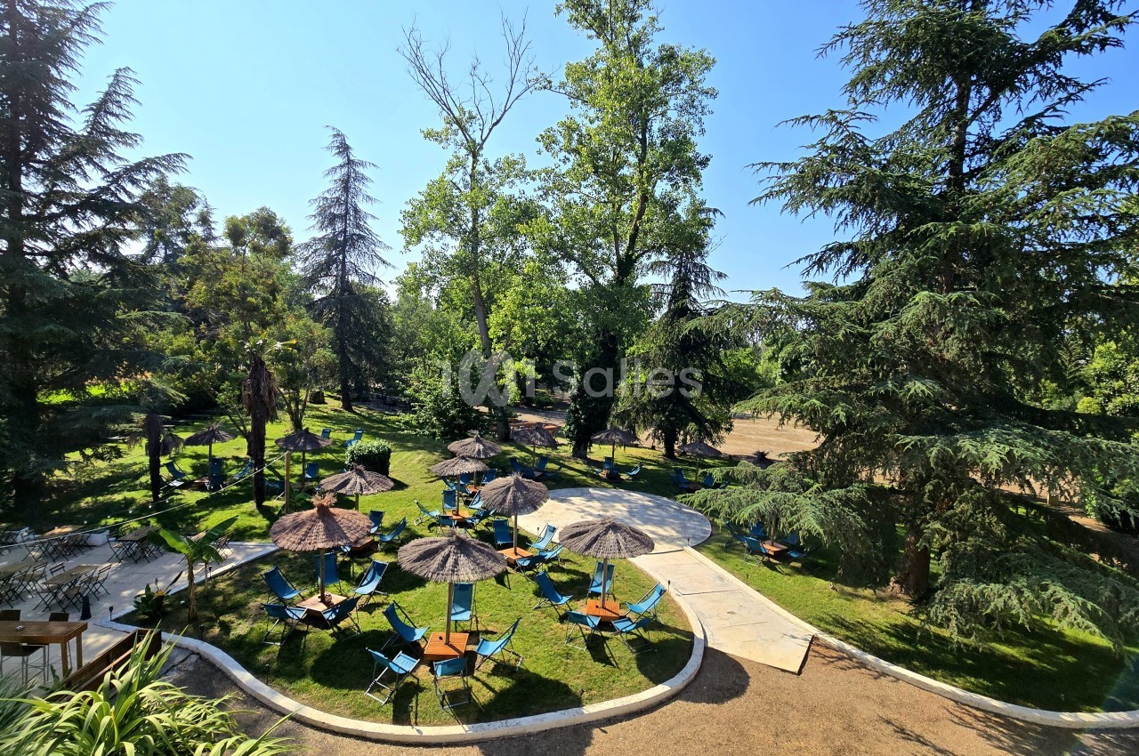 Parc arborisé avec espaces de détente équipés de parasols et chaises longues sous les arbres.