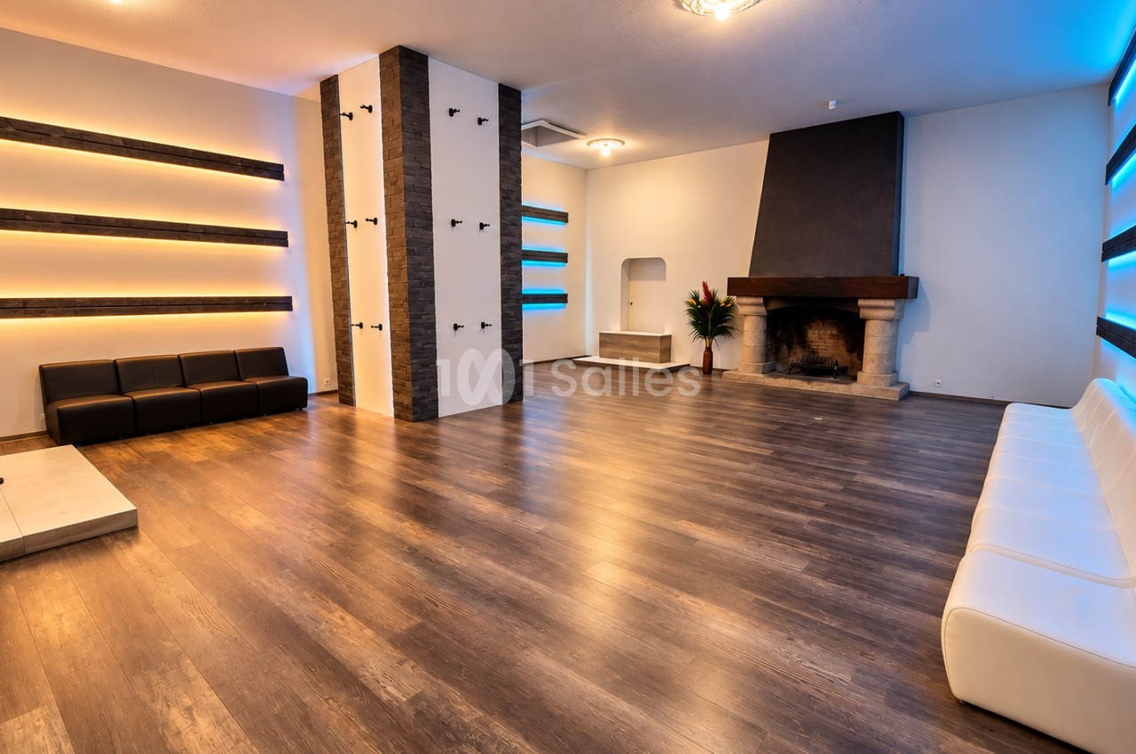 Salle intérieure spacieuse au sol en parquet, colonnes centrales, cheminée, éclairage bleu et orange, mobilier design noir et blanc.
