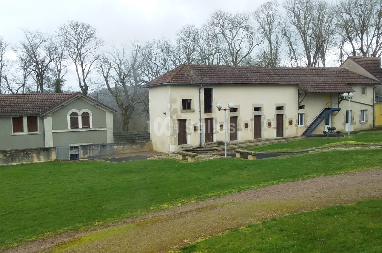 Bâtiment principal de plain-pied aux murs crème avec plusieurs portes - arrière cour en herbe et arbres nus.