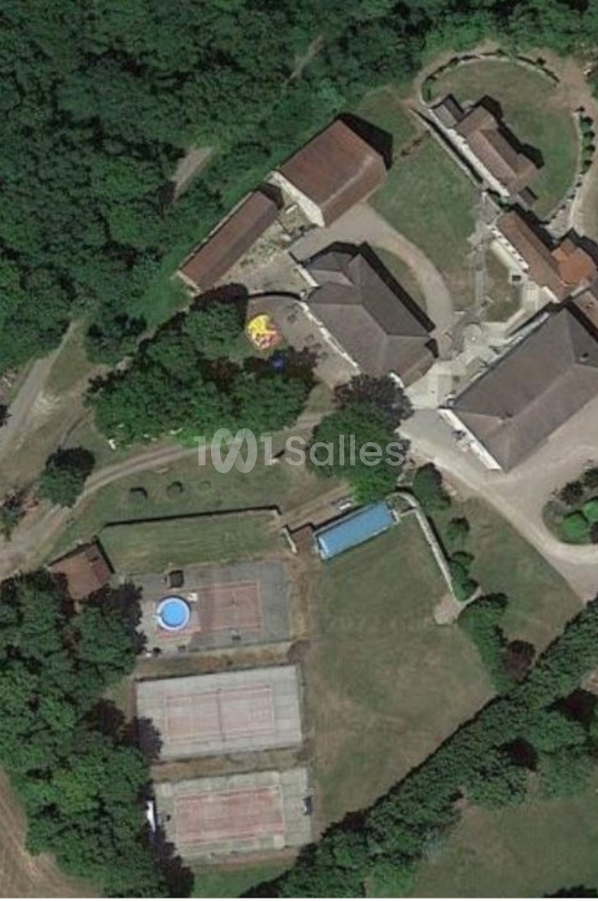 Vue aérienne du domaine avec bâtisses, piscine, court de tennis et espaces verts entourés de forêt.
