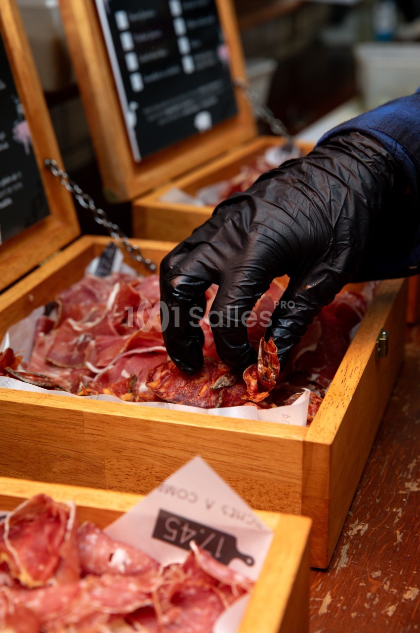 Main gantée de noir présentant une tranche de viande crue dans un bac en bois.