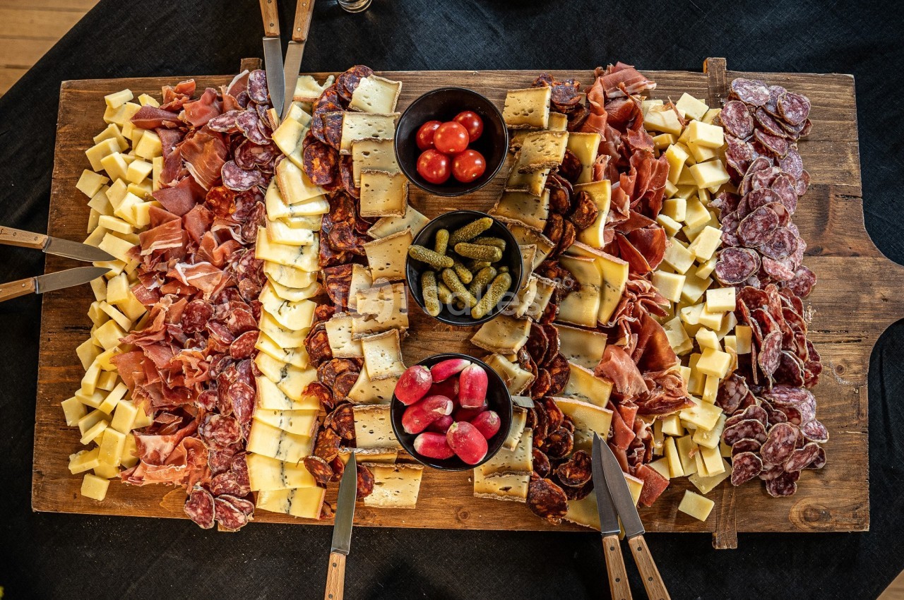 Plateau de charcuterie et fromage sur planche bois avec cornichons et tomates, couteaux à découper.