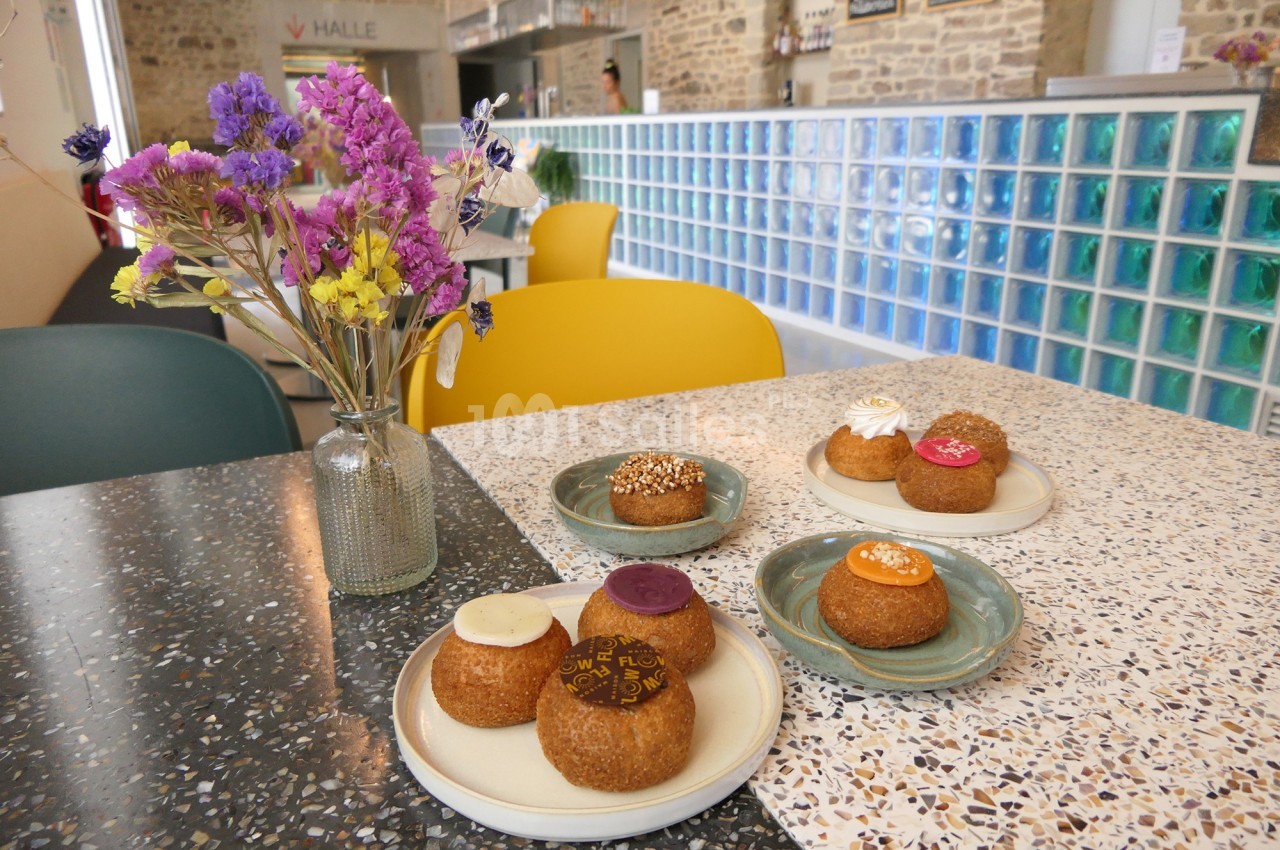 Petites pâtisseries rondes garnies de glaçages colorés sur des assiettes, près d'un bouquet de fleurs séchées.