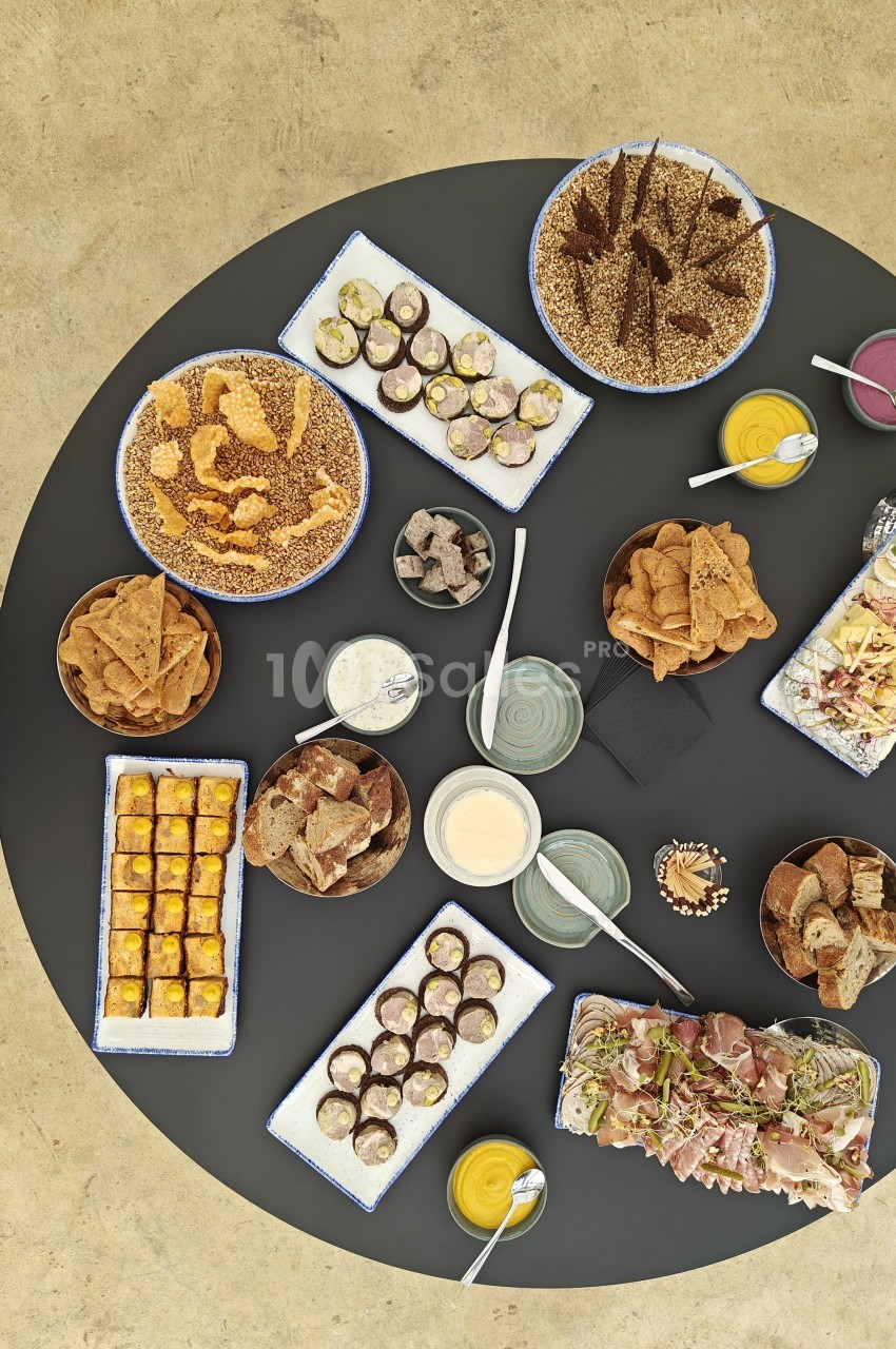 Vue aérienne d'un buffet d'amuse-bouches dressé sur une table ronde sombre : bouchées sur plateaux blancs, chips, pains, sauces dans des coupelles et crudités. Wait, I must not start with "Vue de". Let me rewrite and check length (≤125 chars). Plateau
