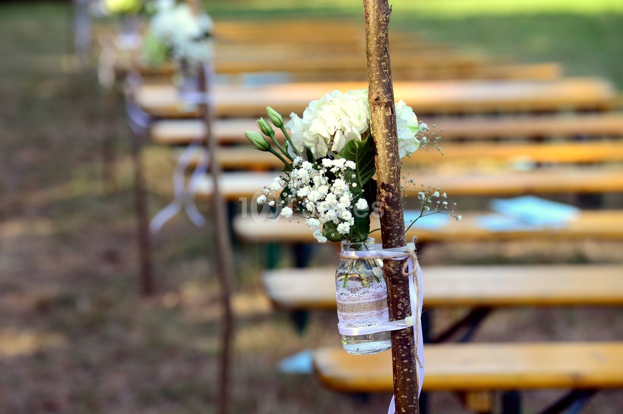 Bouquet blanc et vert fixé à un support en bois, assis sur des bancs en arrière-plan.