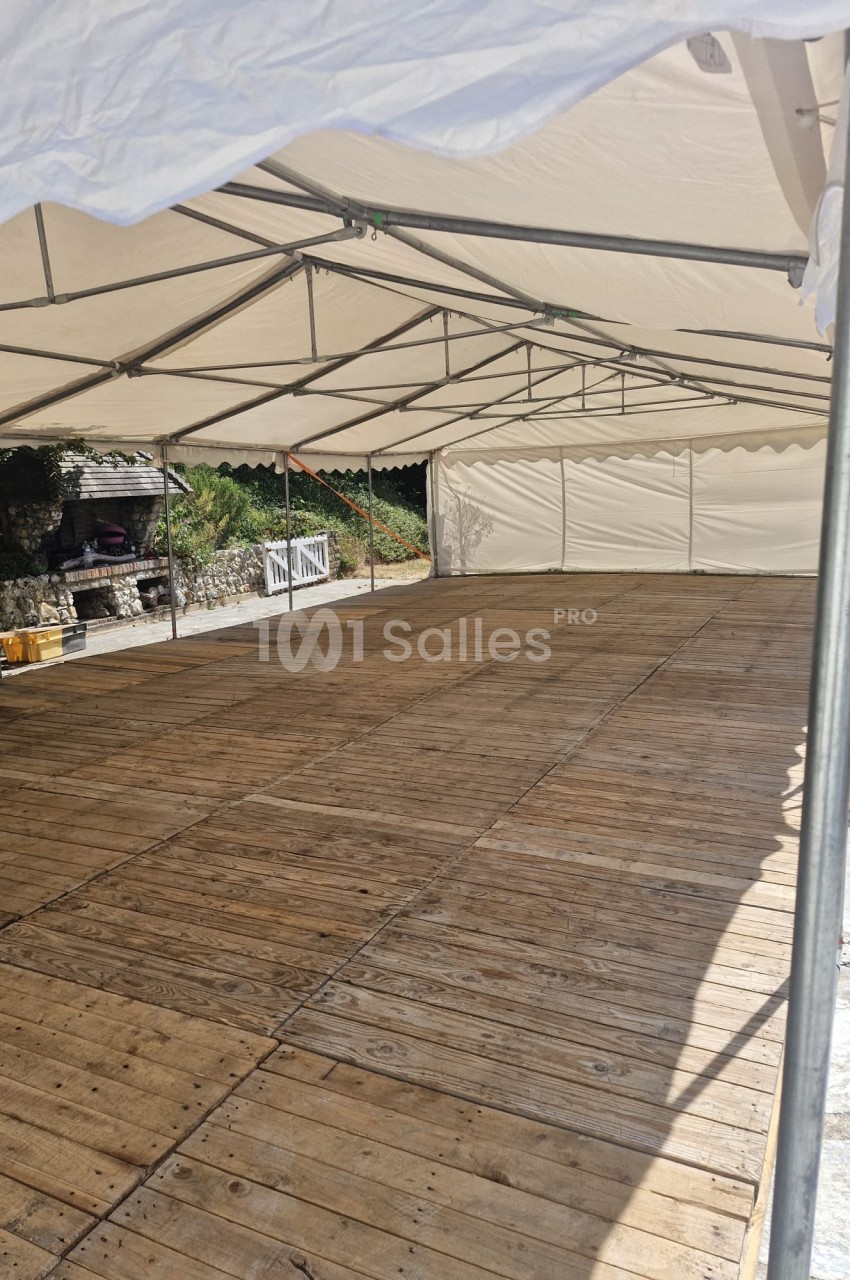Chapiteau avec toile beige, structure métallique apparente et plancher bois, espace vide et ensoleillé.