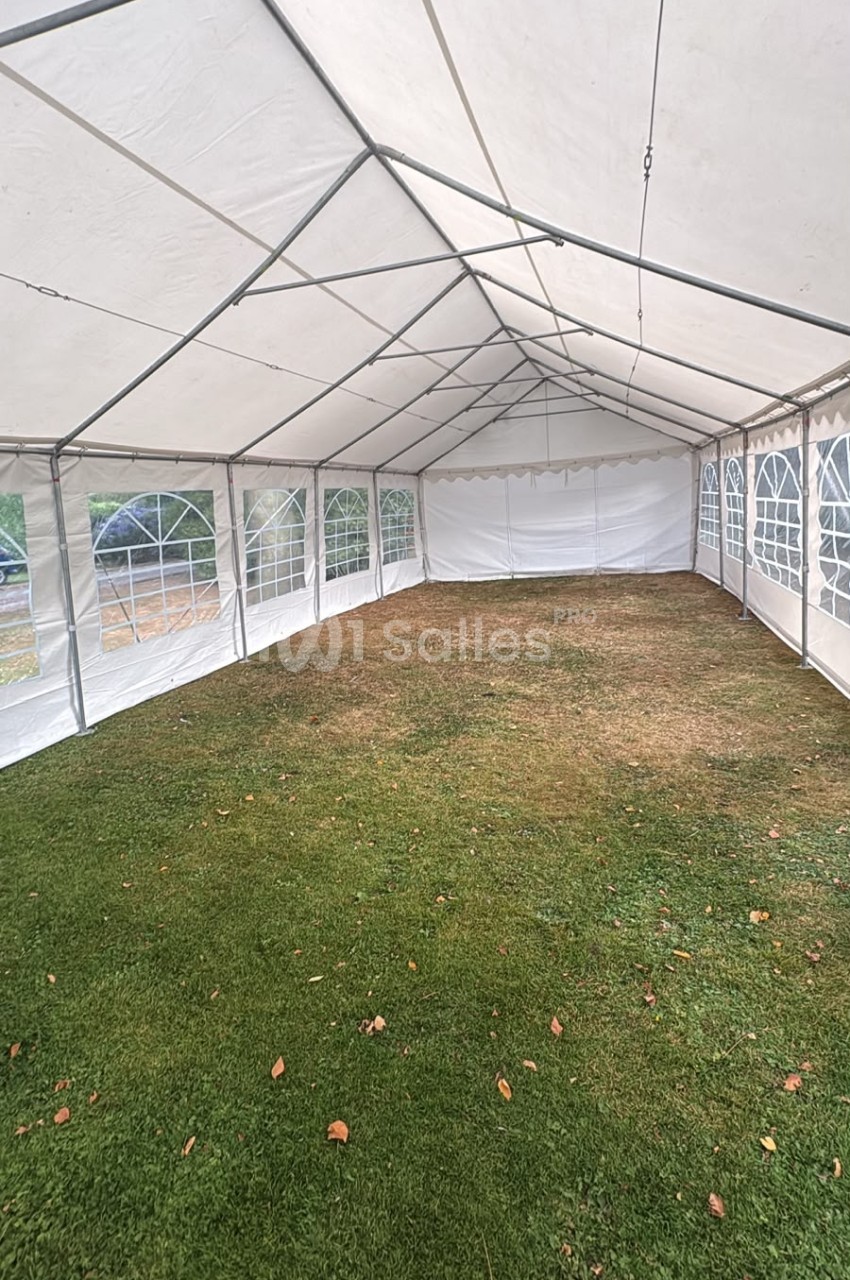 Intérieur d'un chapiteau blanc vide avec sol en herbe, parois transparentes et structure métallique.