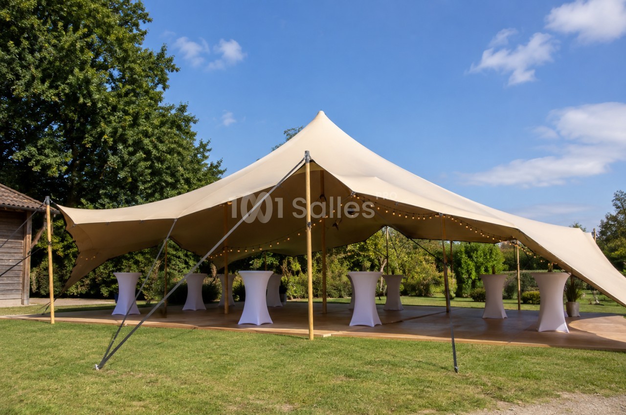 Chapiteau blanc dressé en plein air avec tables hautes blanches, entouré de verdure.