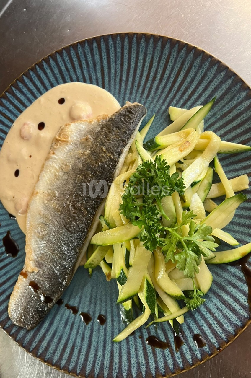 Filet de poisson grillé à la peau croustillante, servi sur une purée crémeuse et accompagné de fines lanières de courgette et de persil frais, sur une assiette bleue.