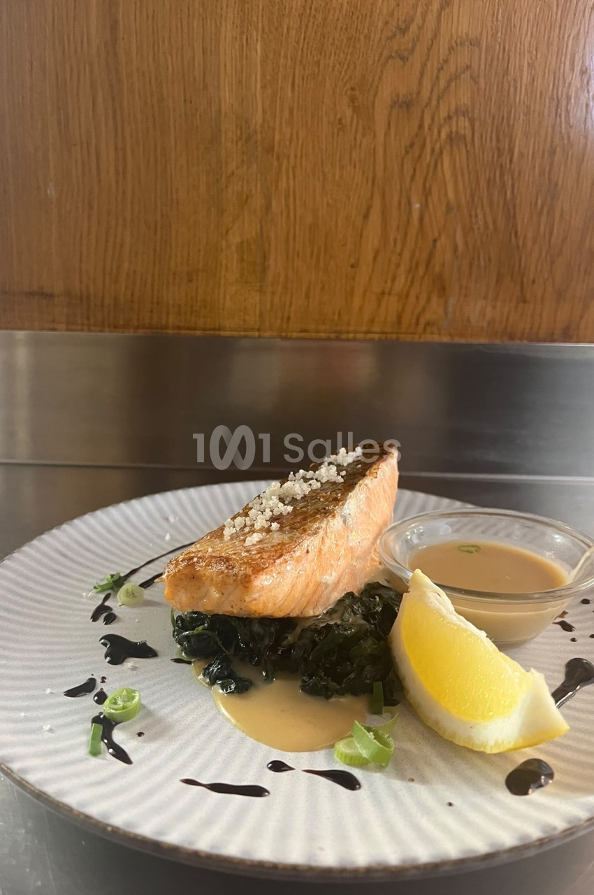 Pavé de saumon snacké posé sur des épinards, accompagné d'une sauce crémeuse, d'un quartier de citron et de ciboulette fraîche.