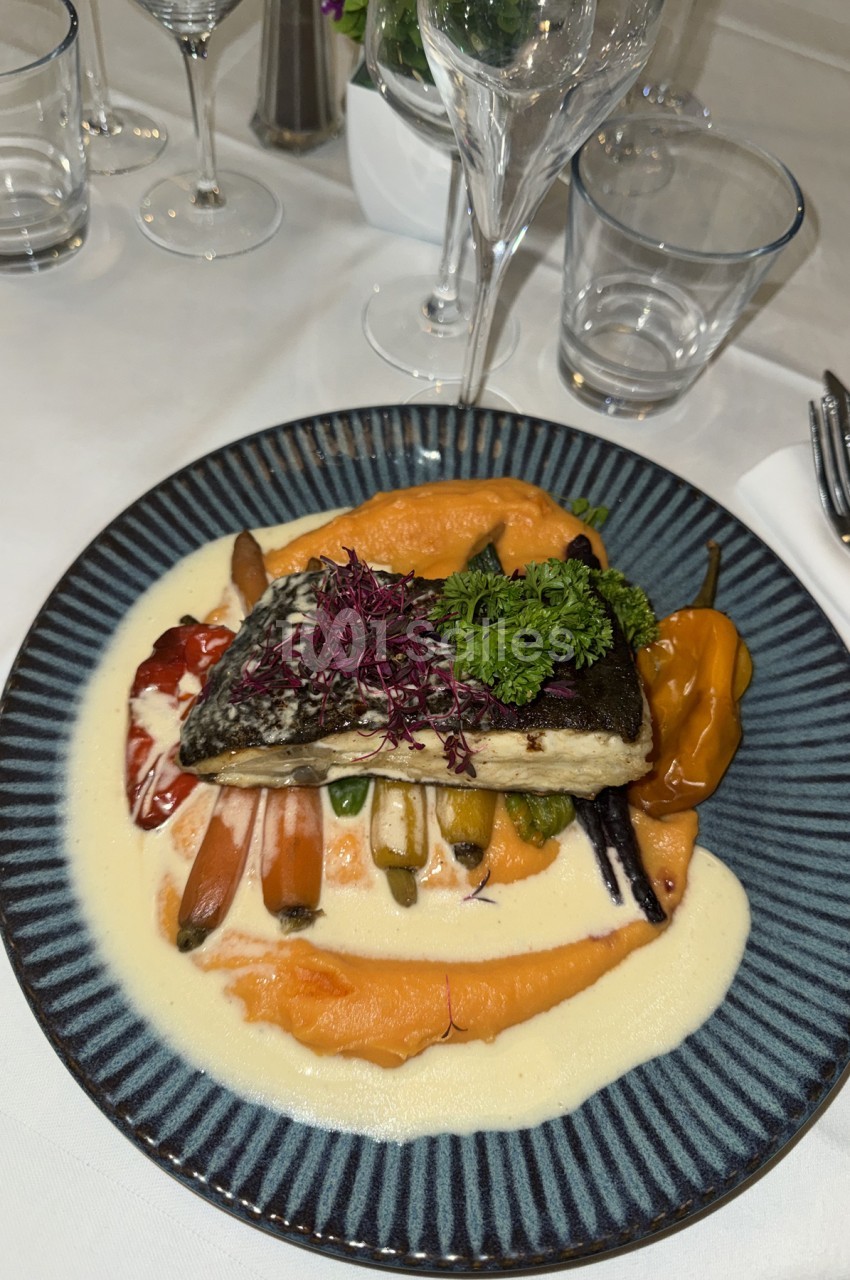 Pavé de poisson à la peau croustillante posé sur une purée orangée et une crème blanche, accompagné de légumes colorés et de persil frisé, servi dans une assiette bleue striée.