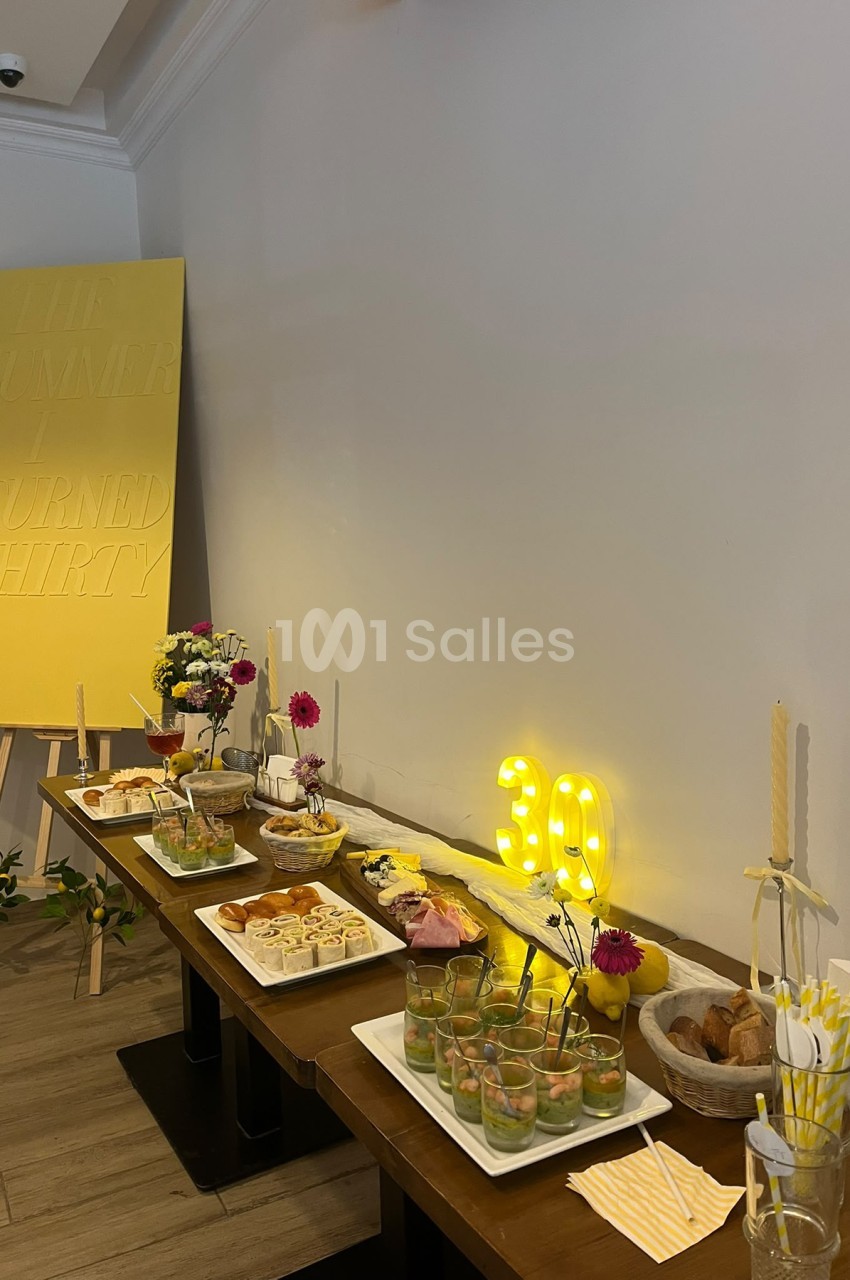 Buffet apéritif dressé sur une table en bois : verrines, roulés, pains, charcuterie et chiffres lumineux 30 en décor jaune.