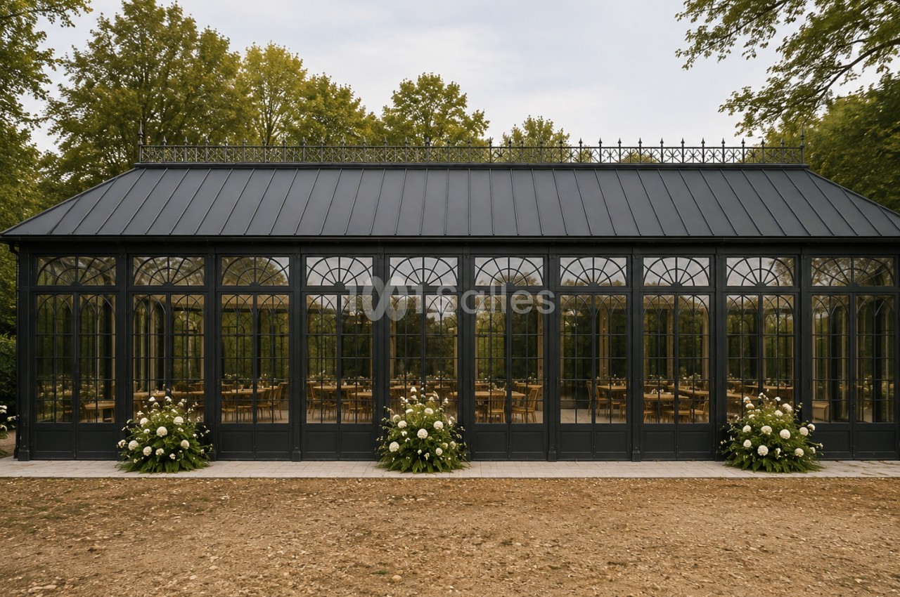 Orangerie noire aux baies vitrées cintrées, tables dressées à l'intérieur, entourée d'arbres et d'hortensias blancs.