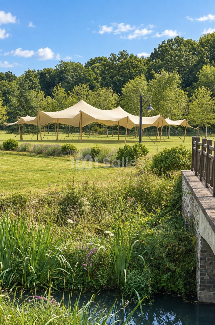 Grand tente structure beige aux mâts en bois, dressée sur une pelouse bordée d'arbres, avec un pont en brique et un canal au premier plan. Hmm, "Grand" est incorrect : il faut "Grande tente". Corrected version: Grande tente toile beige aux mâts en bois