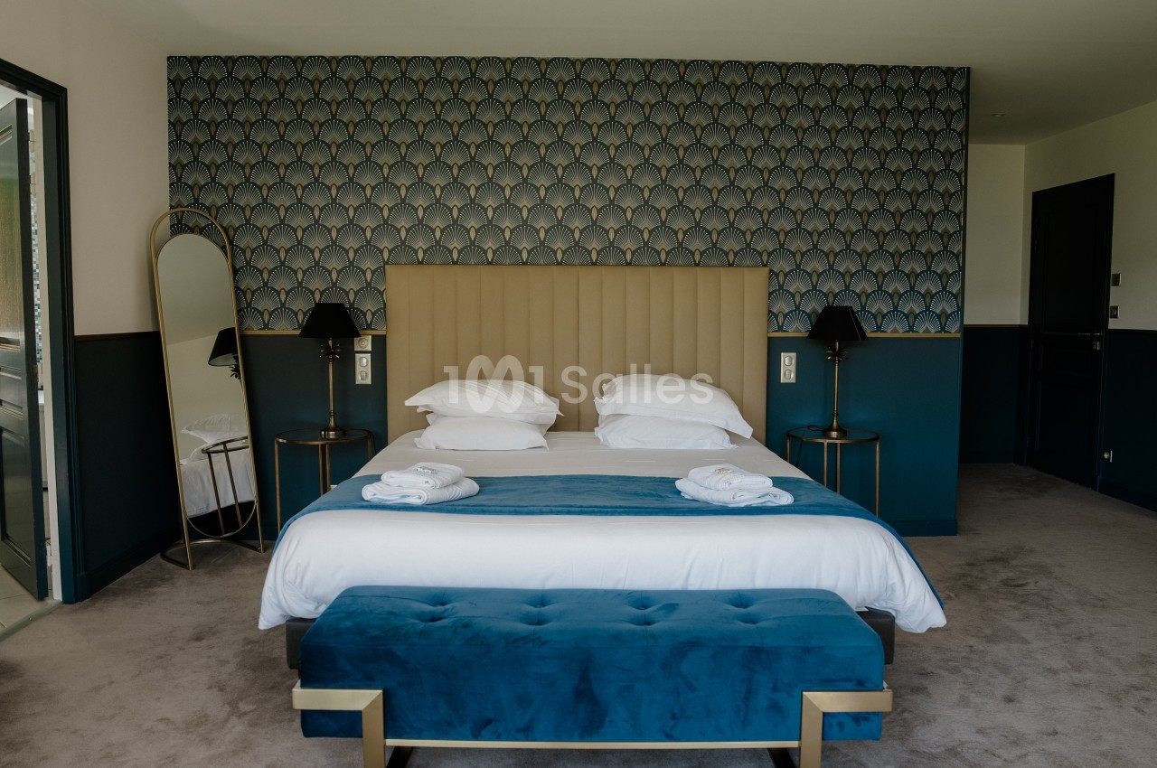 Chambre d'hôtel avec un grand lit blanc, une tête de lit capitonnée beige, un papier peint à motif d'éventails bleu et doré, et un banc bleu velours au pied du lit. Wait: the output must be a single sentence, ≤125 characters. The above is too long. Let