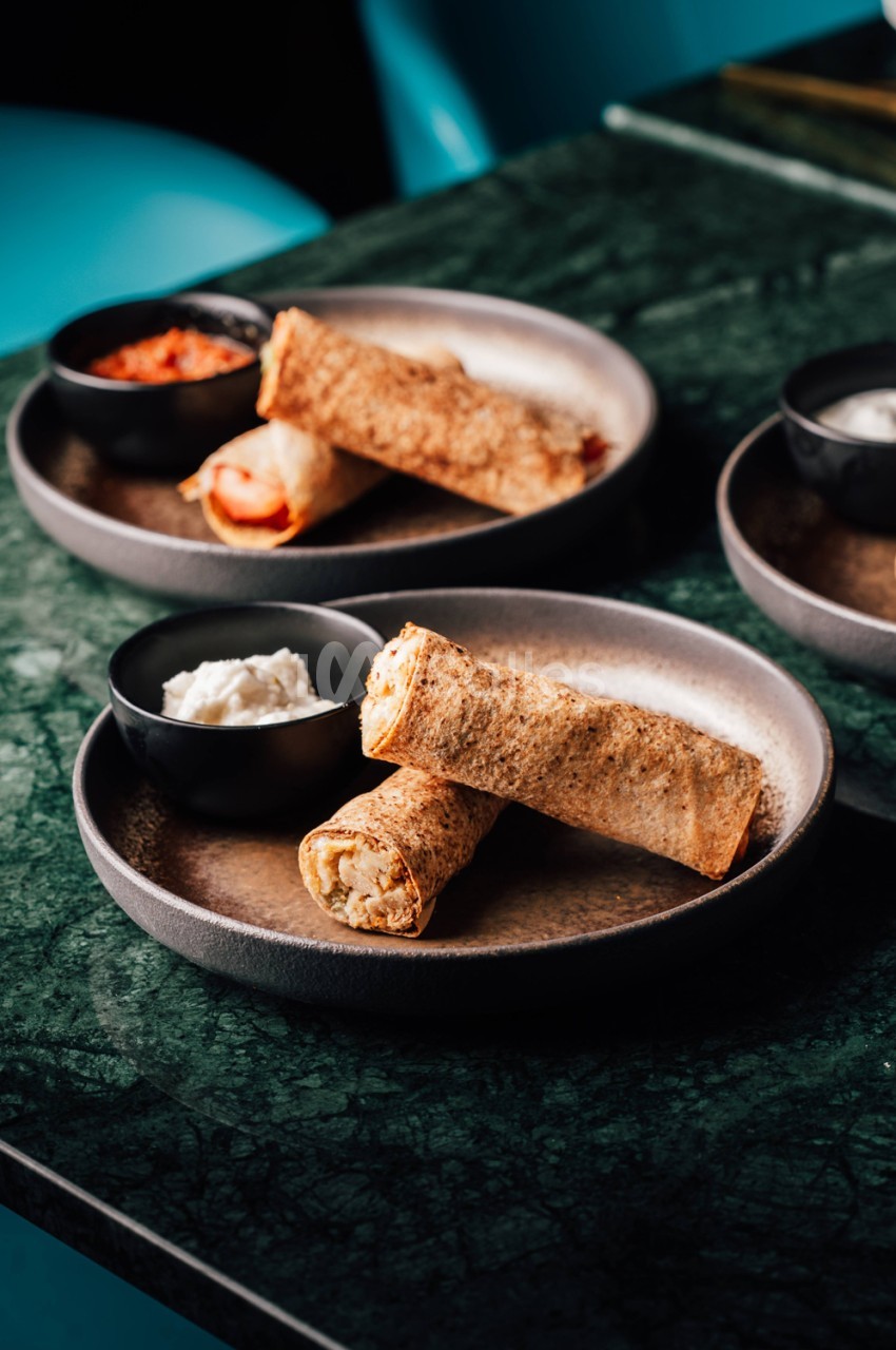 Crêpes roulées garnies accompagnées de sauces et crème fraîche en petits bols noirs.