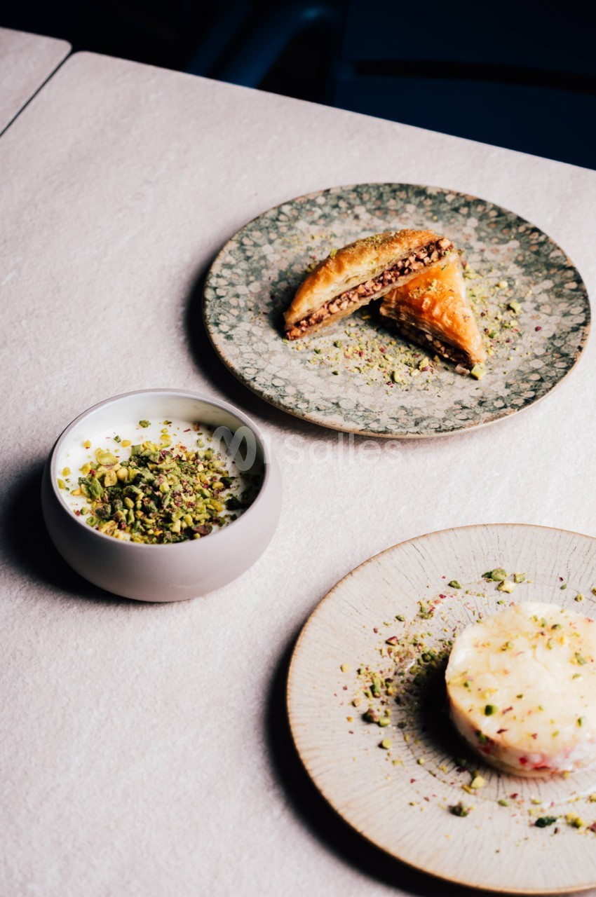 Trois assiettes de pâtisseries aux pistaches et garnitures crémeuses sur nappe blanche.