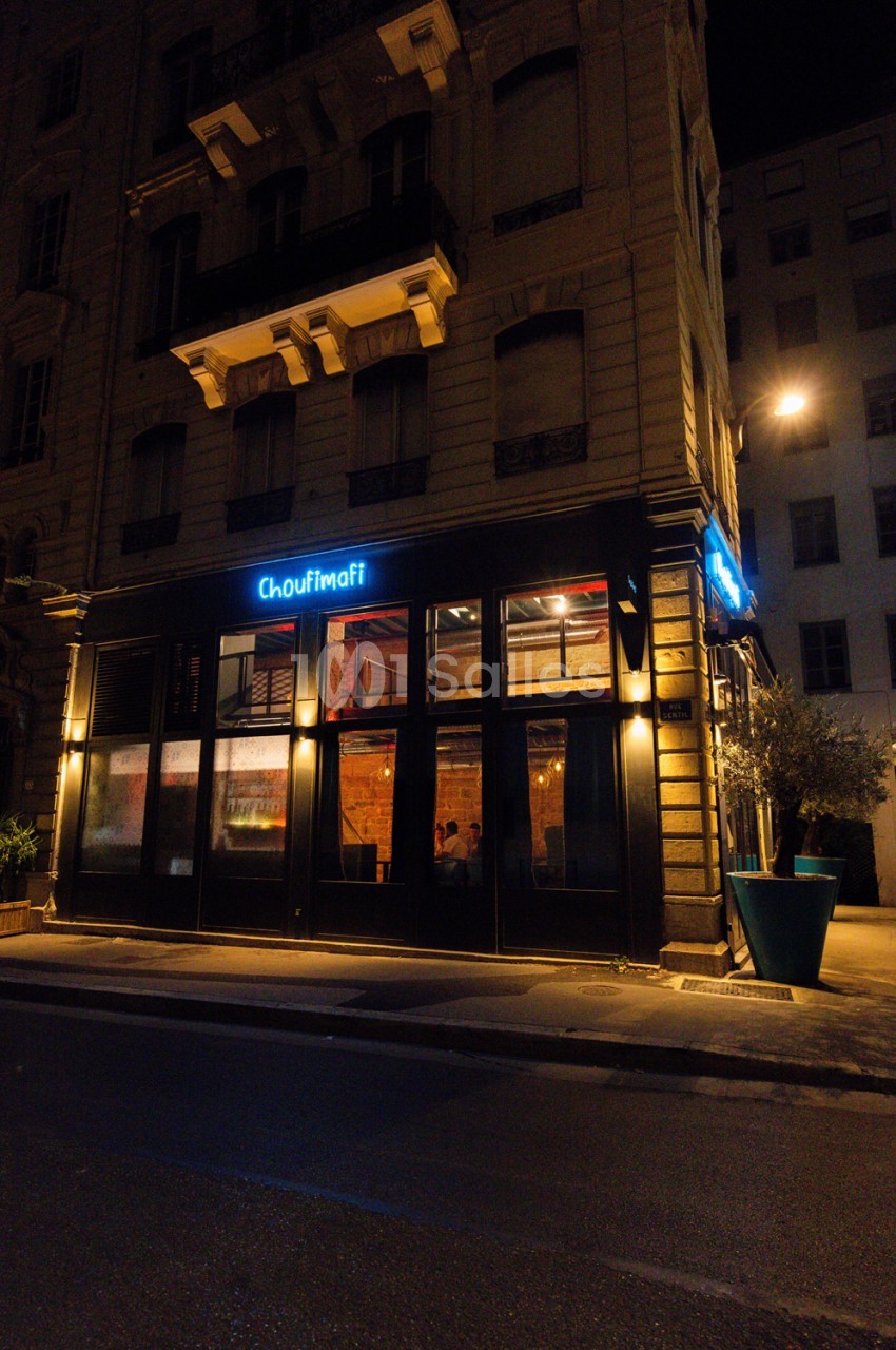 Façade vitrée de restaurant illuminée la nuit, enseigne bleue Choufimafi, bâtiment haussmannien en pierre à l'arrière-plan.