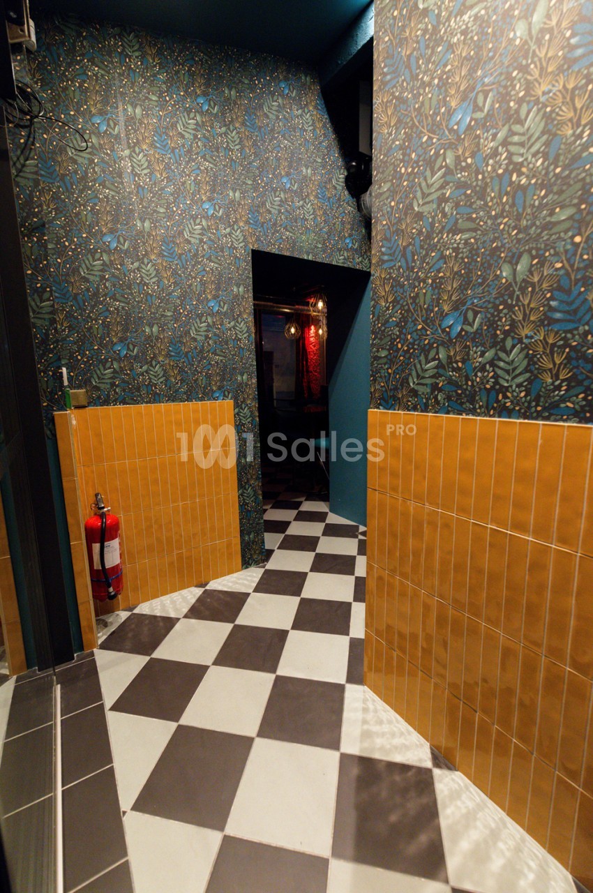 Couloir de circulation aux murs tapissés de motifs floraux bleus et or, carrelage damier noir et blanc, boiseries orange sur les parois basses.