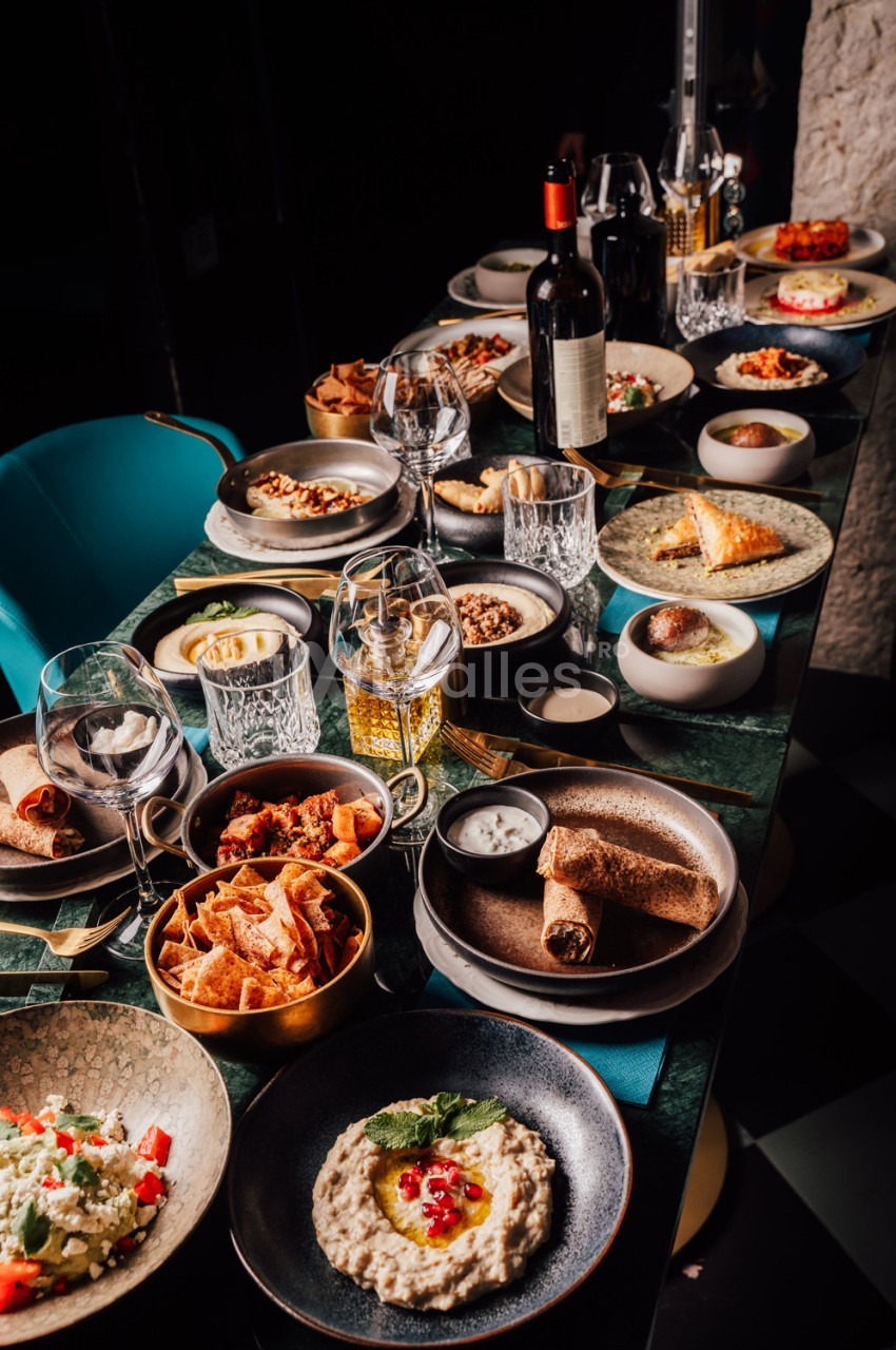 Table dressée avec chaises turquoise, plats cuisinés variés, verres et bouteilles de vin - ambiance repas gastronomique.