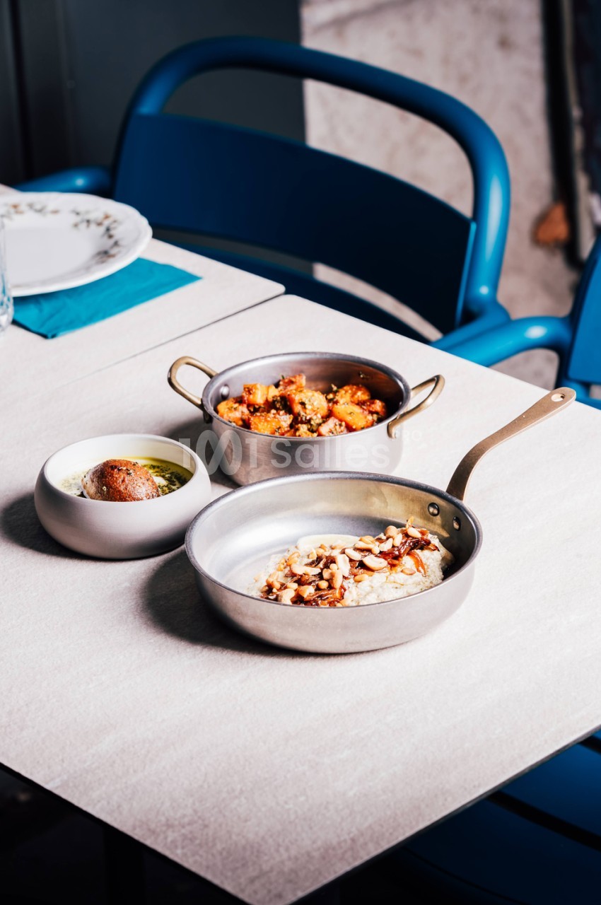 Table dressée avec trois plats en cocotte et poêle - légumes rôtis, préparation crémeuse et riz aux amandes - chaise bleue en arrière-plan.