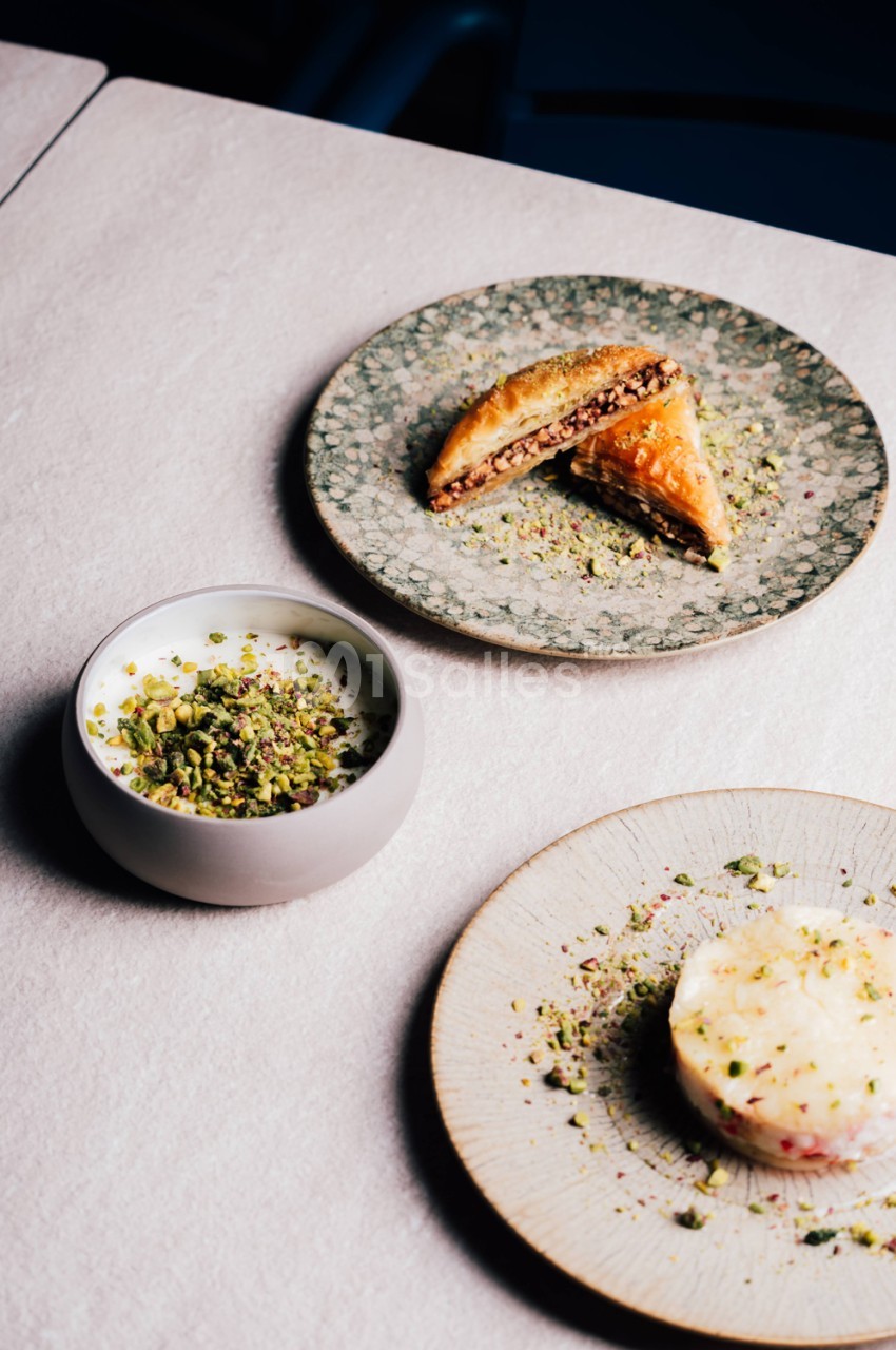 Trois assiettes de pâtisseries aux pistaches et garnitures crémeuses sur nappe blanche.
