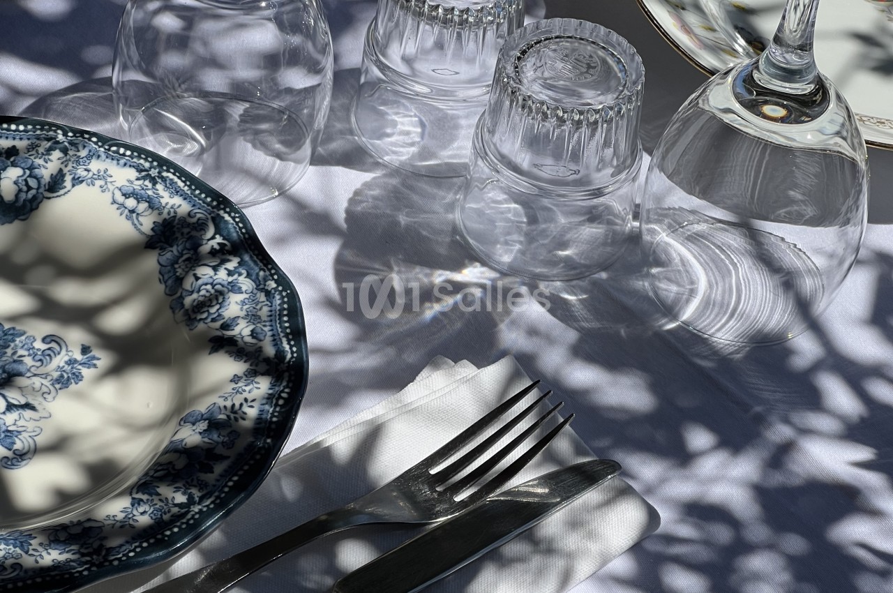 Couvert dressé avec assiette à motifs bleu et blanc, couverts noirs et verres vides sur nappe blanche.