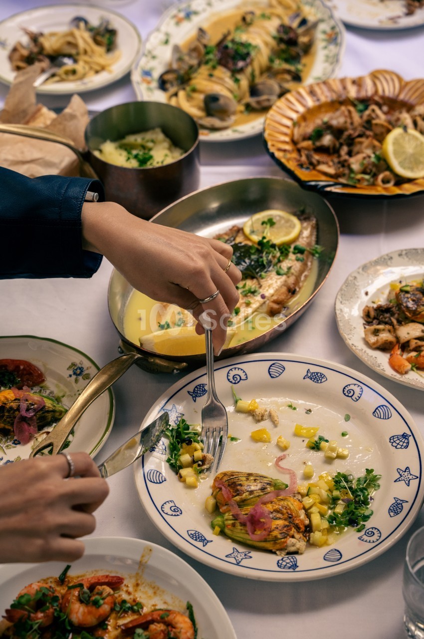 Table dressée avec fruits de mer, pâtes et poissons garnis de citron et persil - convives en train de manger.
