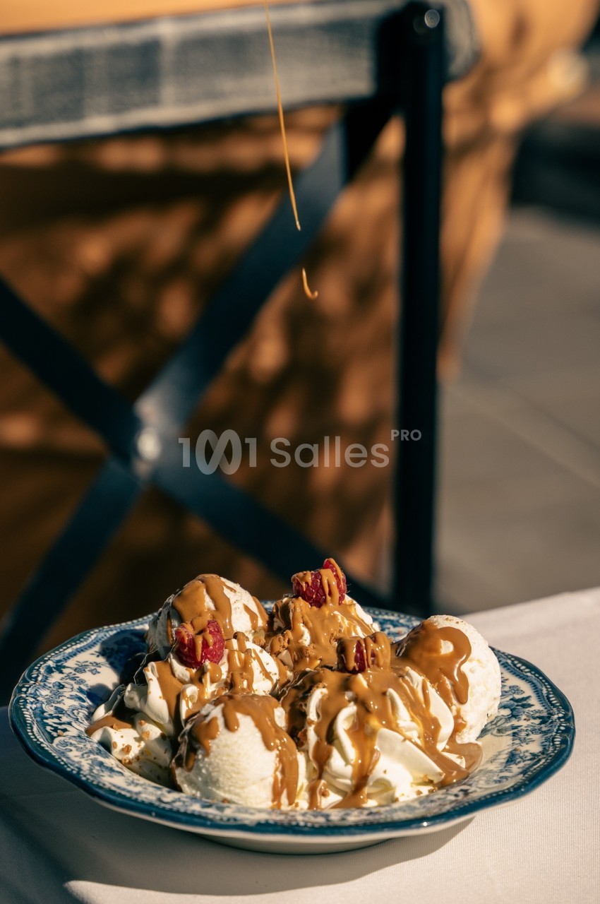 Assiette de boules de glace vanille nappées de caramel et bacon croustillant en terrasse ensoleillée.