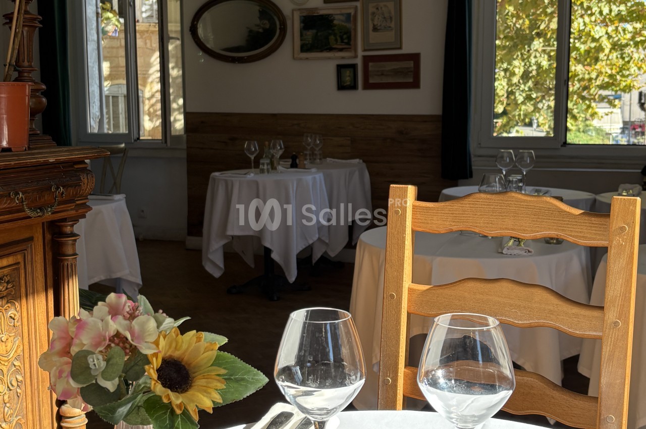 Salle de restaurant avec tables rondes dressées, chaises en bois clair et vues sur verdure depuis larges fenêtres.