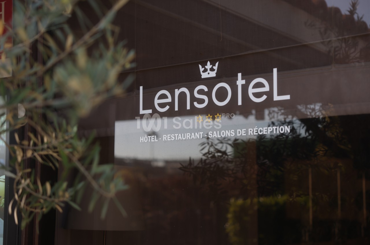 Vitrine d'un établissement avec le logo « Lensotel » surmonté d'une couronne, indiquant hôtel, restaurant et salons de réception, feuillage d'olivier au premier plan. Hmm, the alt must not transcribe text embedded in the image (enseigne, affiche). The